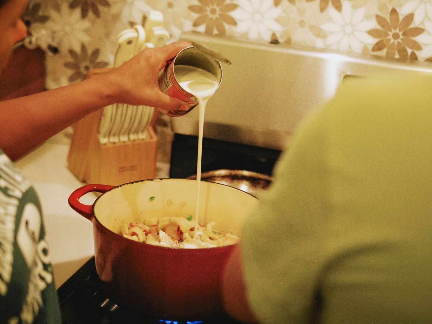 Person pouring cream into a red Dutch oven pot on a stovetop while cooking a savory dish.
