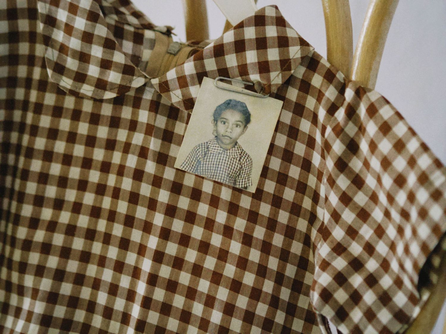 Brown and white gingham shirt on a chair with a vintage school photo of a young child pinned to the pocket.