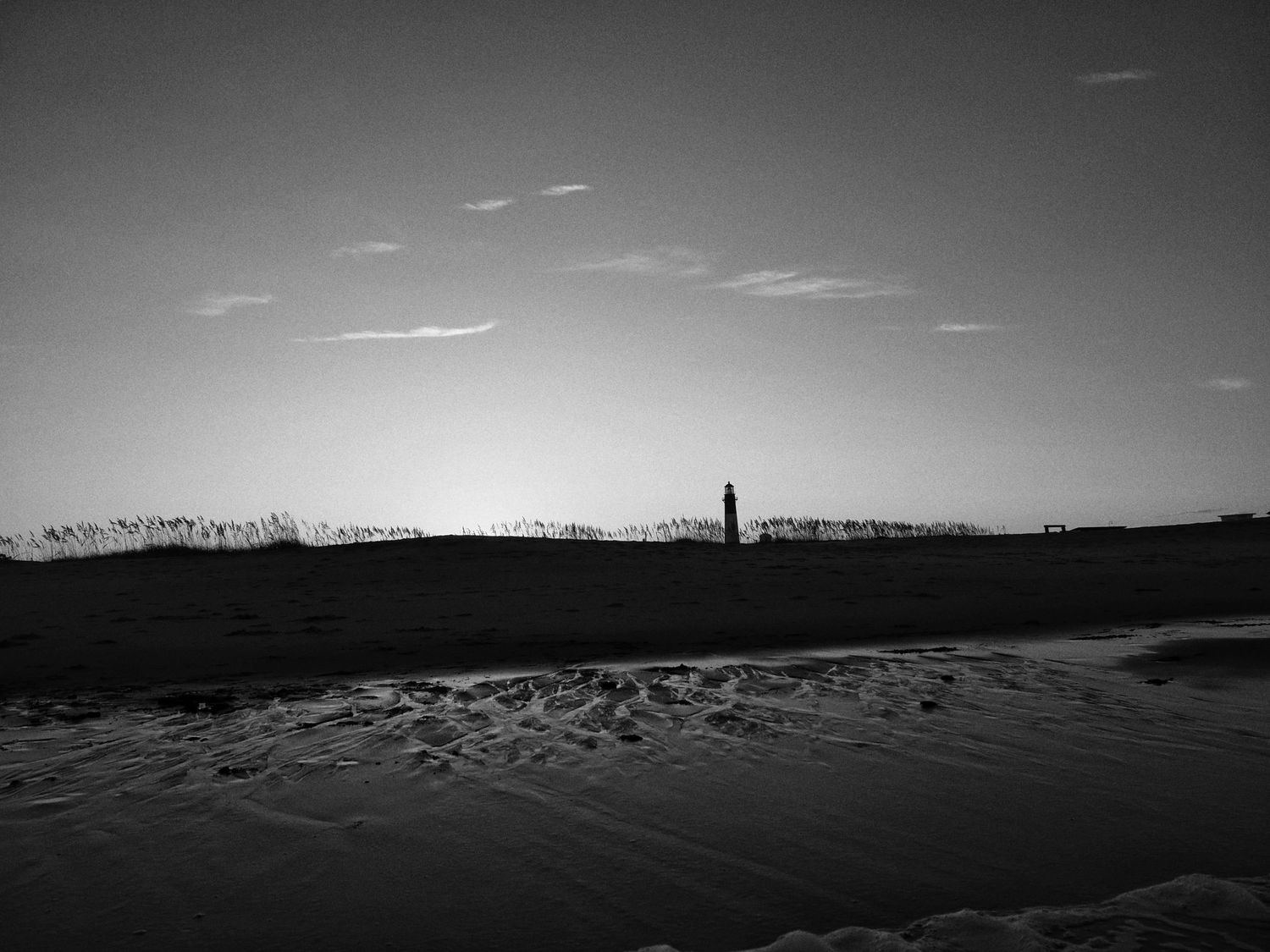 A black and white panoramic series showing a coastal lighthouse silhouette against a dramatic cloudy sky.