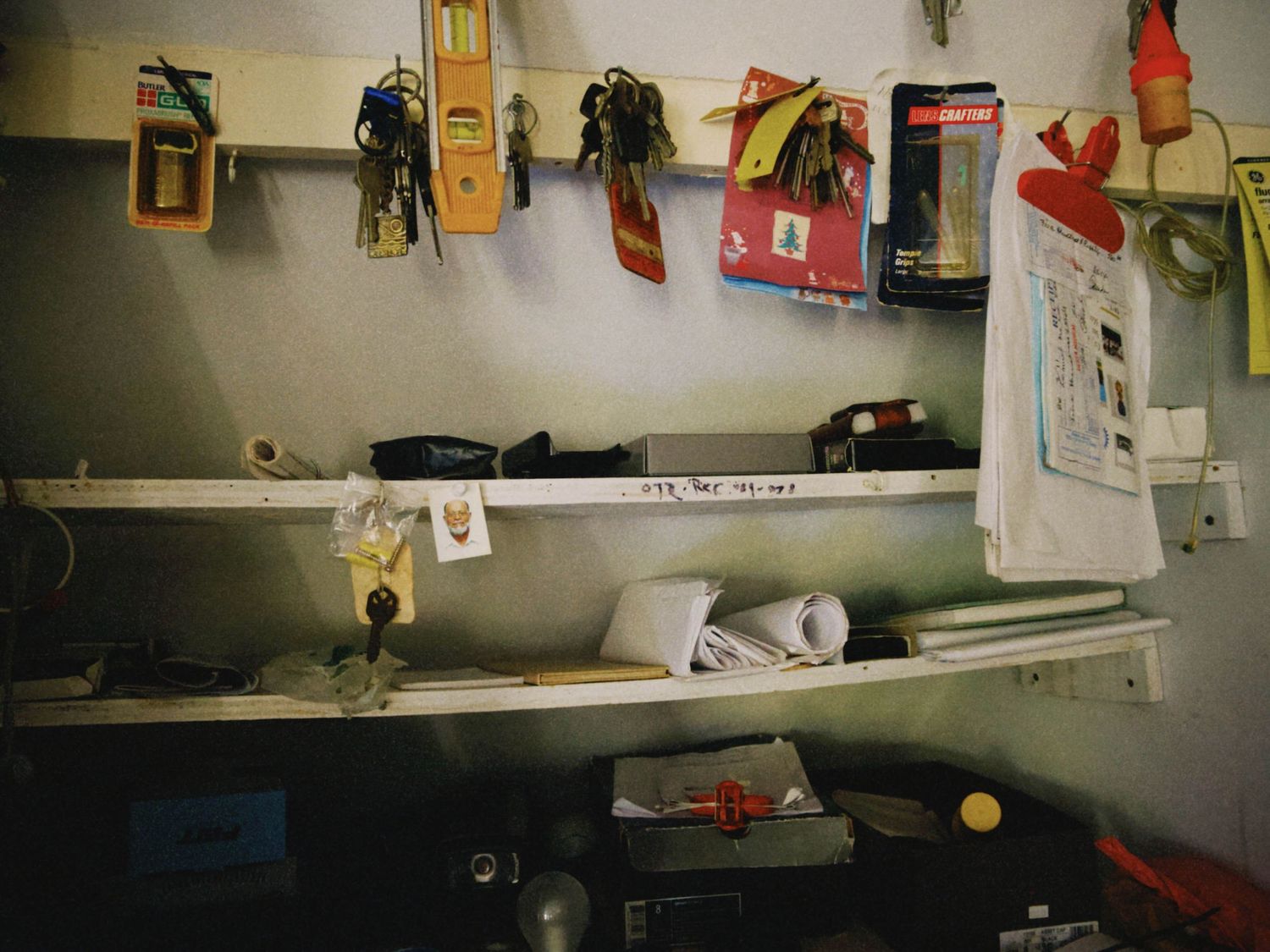 Cluttered garage workshop wall with shelves holding tools, papers, and equipment including a level and various hand tools.