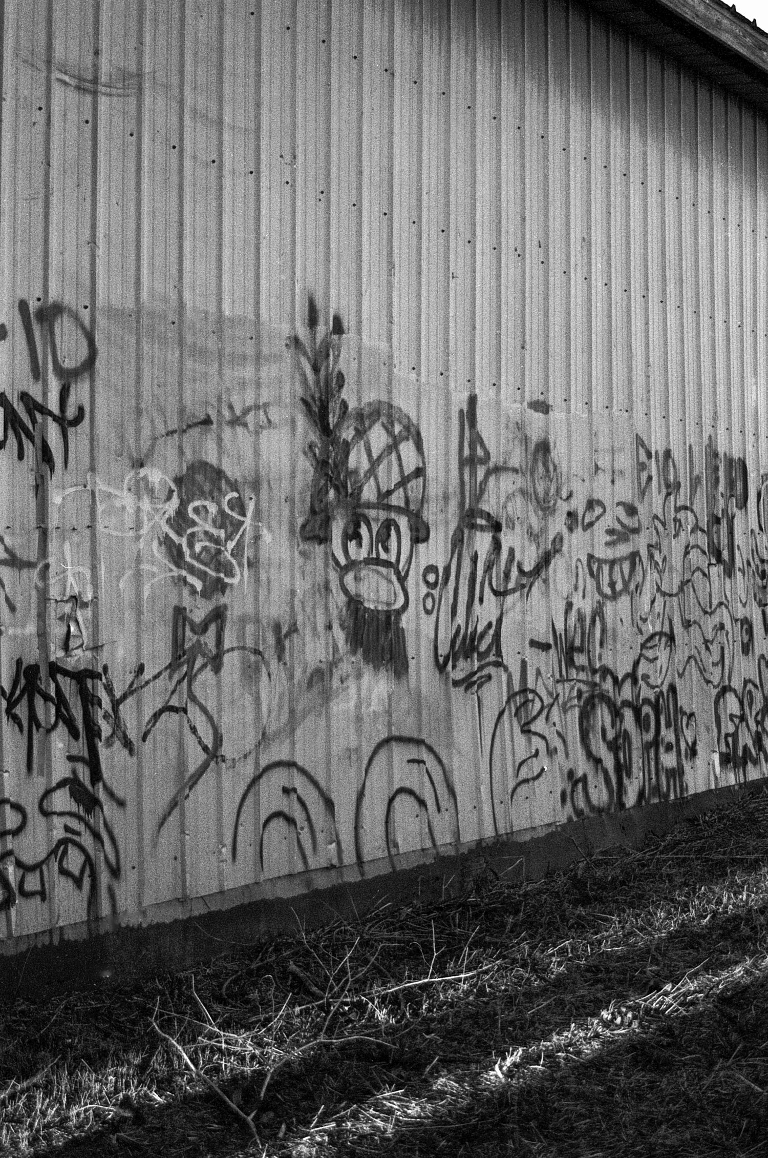 Black and white photograph of graffiti art covering a long concrete wall with dark shadows cast on the ground.