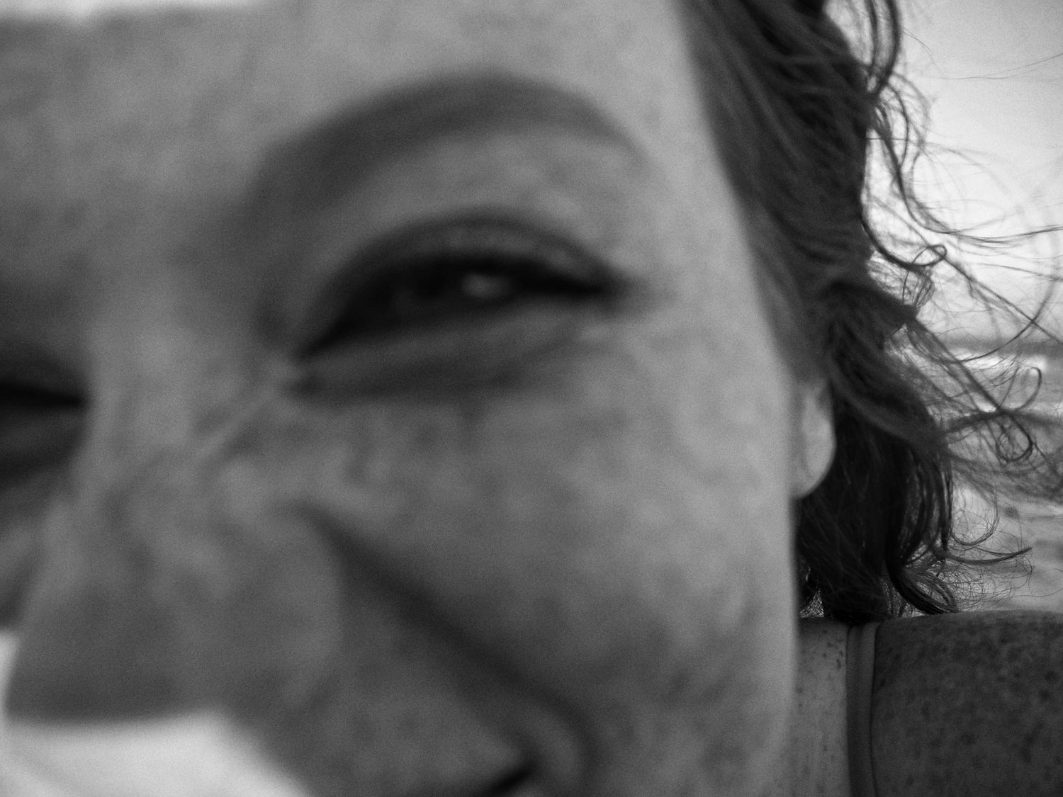 A close-up black and white photograph showing a person's eye and part of their face in dramatic lighting.