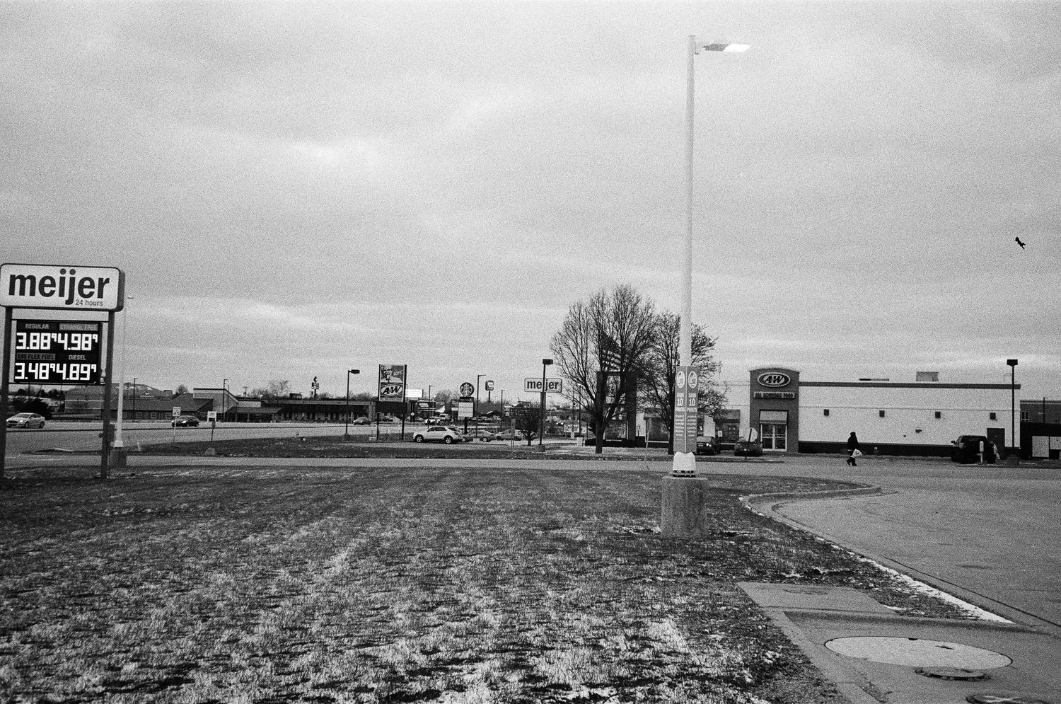 A black and white panoramic view of a commercial strip with a Meijer store and other retail buildings along a highway.