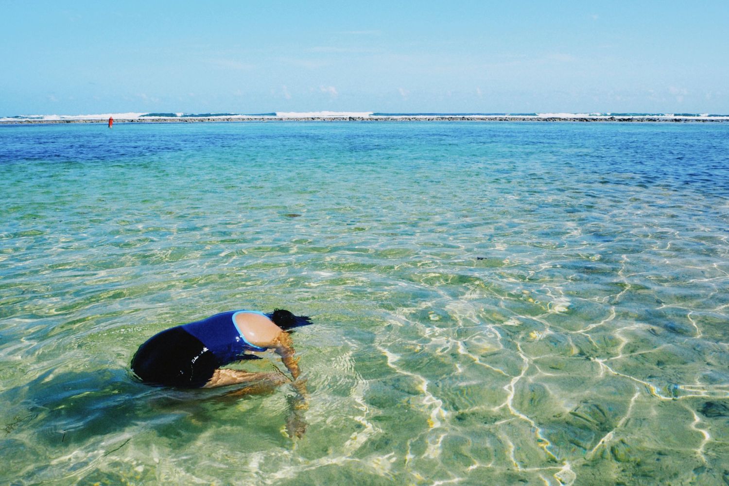 Person in blue swimsuit floating face-down in clear turquoise shallow tropical ocean water.