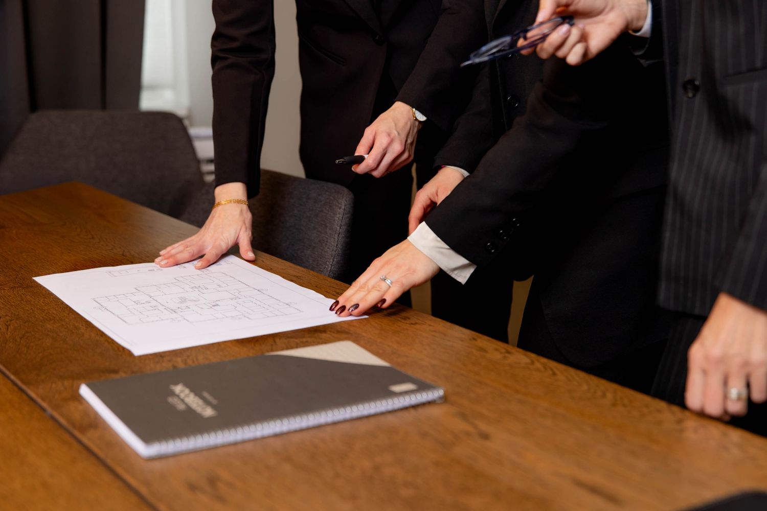 Professional hands gesturing over documents and laptops during a business meeting at a wooden conference table.