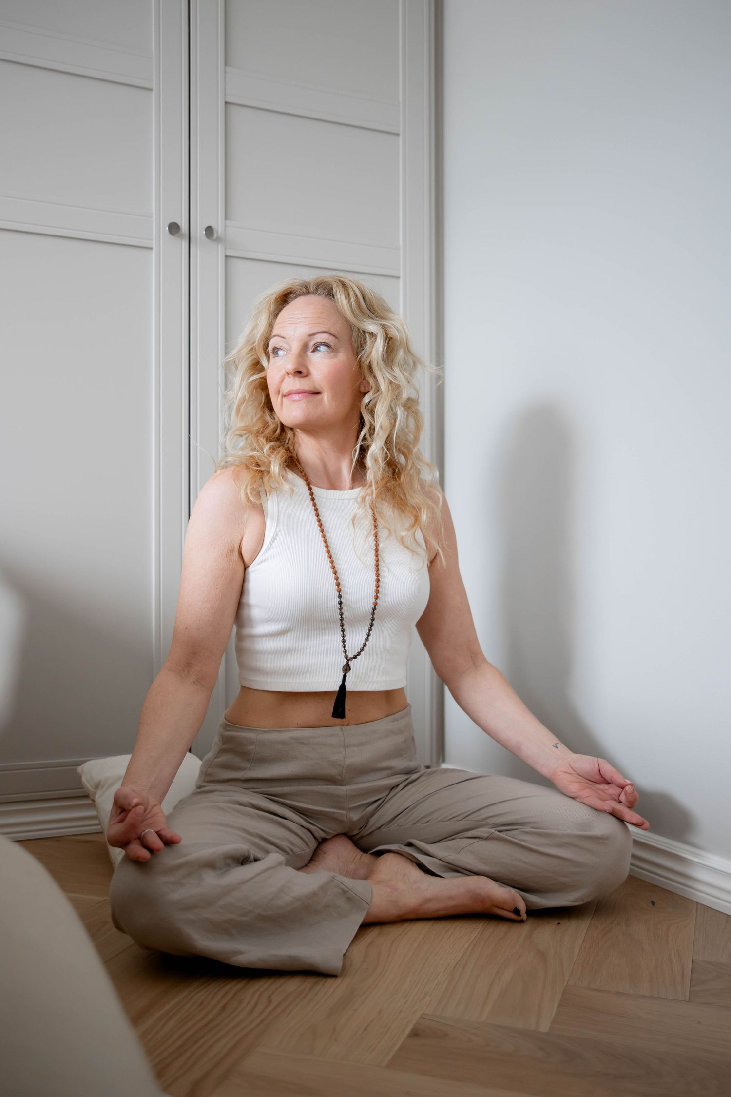 A person in a white tank top and beige pants sits on a wooden floor against a white wall in a series of poses.