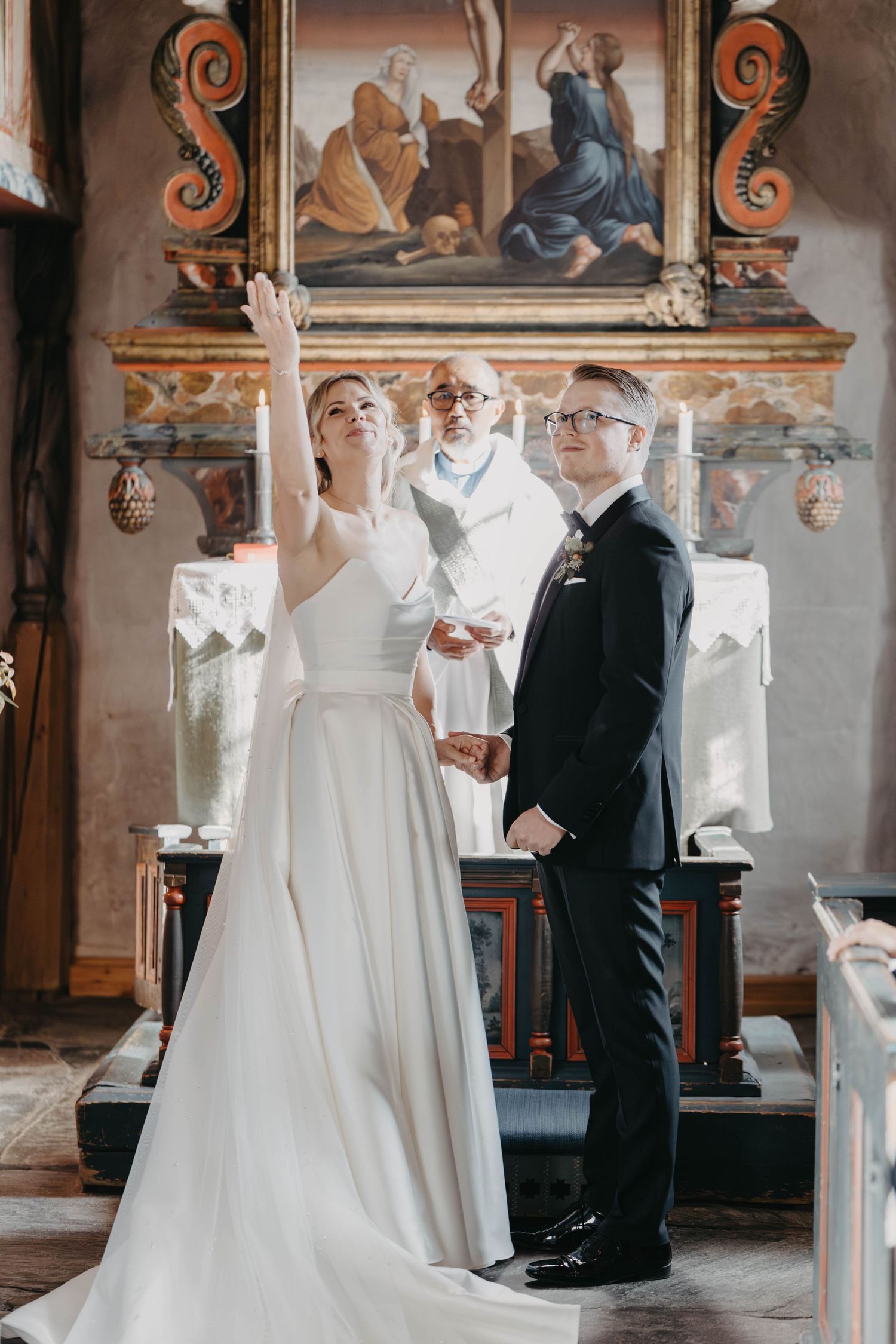 A wedding ceremony takes place in a historic church with ornate decorations and religious artwork on the altar.