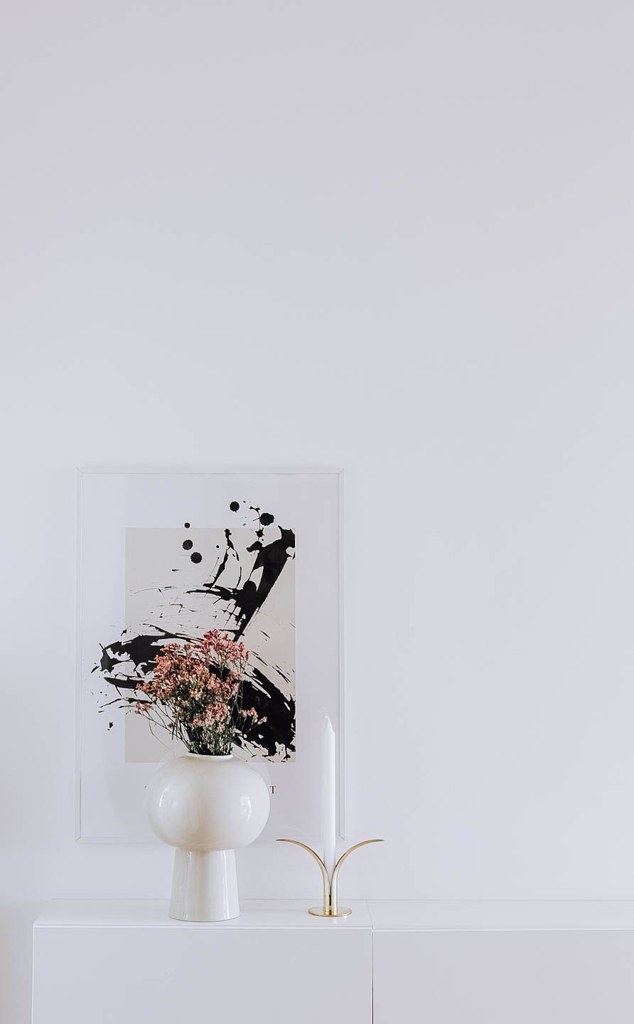 Minimalist white vase with abstract black and pink splatter artwork displayed on light surface.
