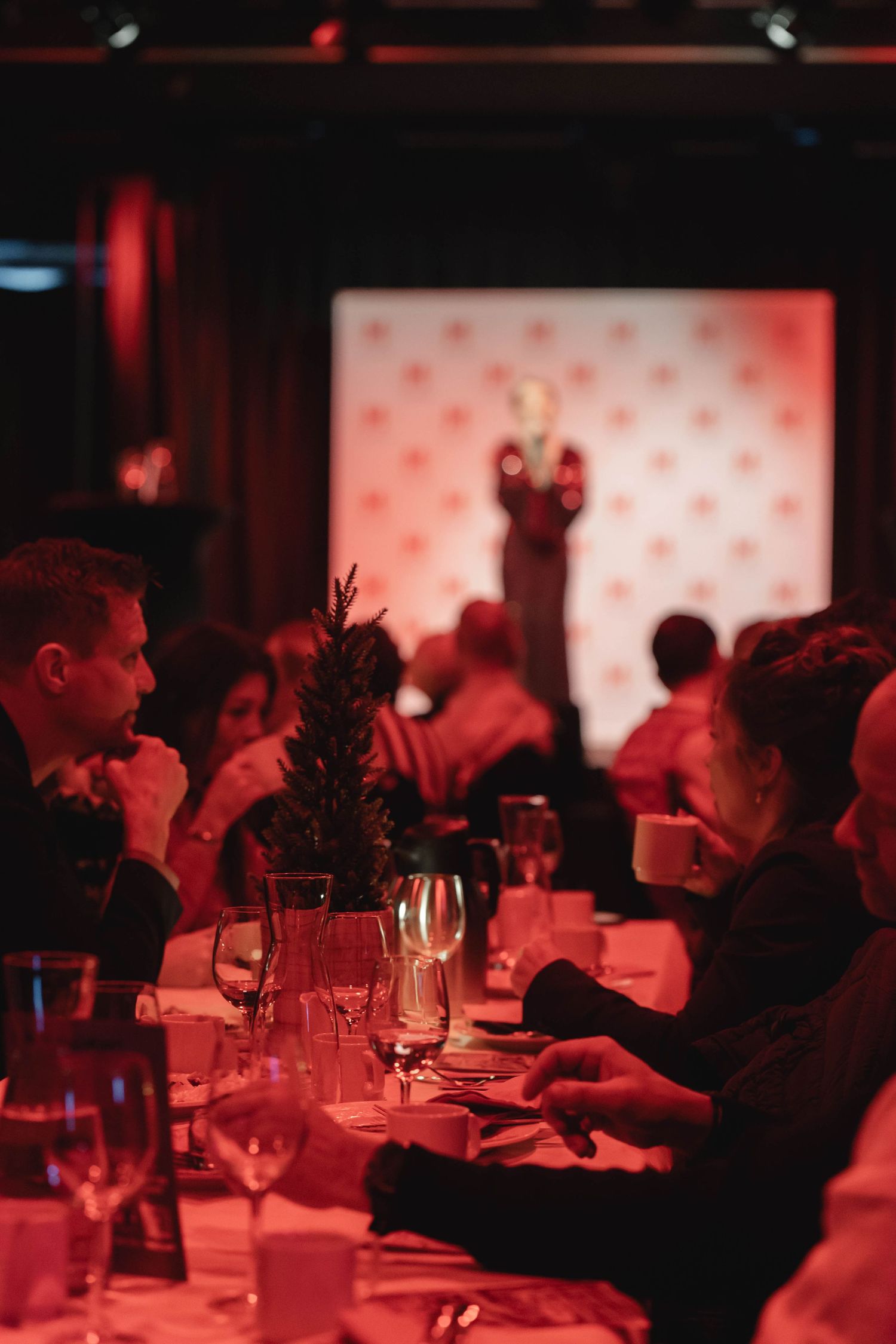 Guests dining at an elegant restaurant with red ambient lighting and wine glasses on tables.