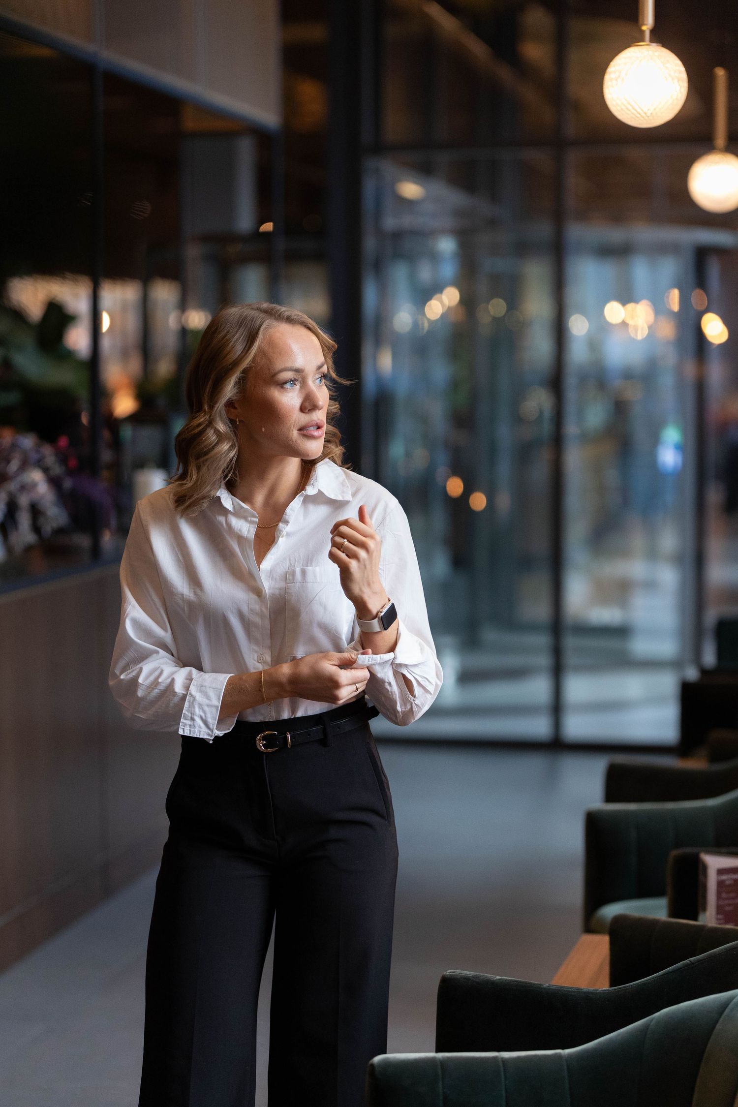 Professional woman in black and white attire sits thoughtfully in modern office space with ambient lighting.