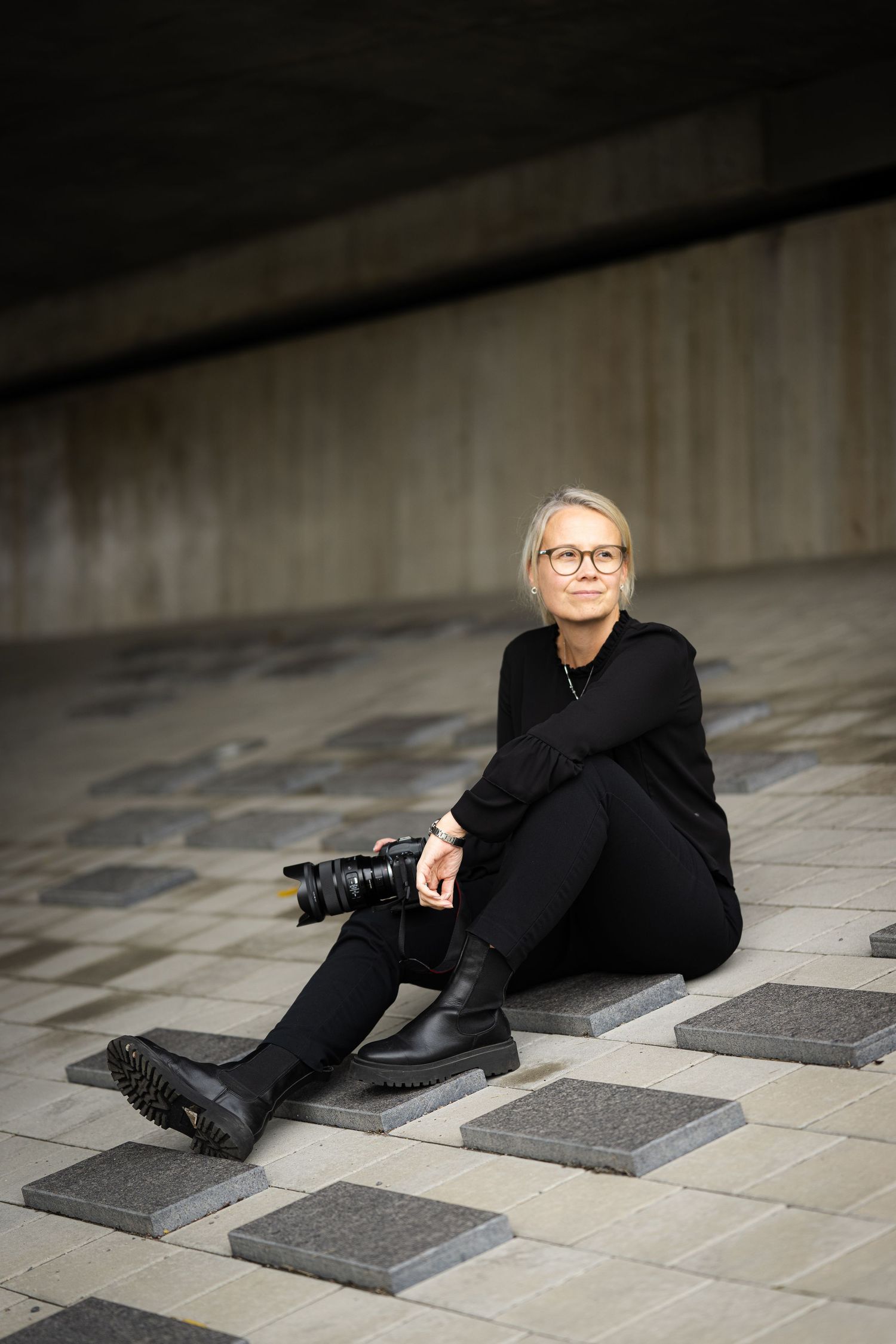 A person in black attire and glasses lying on a tiled floor with geometric patterns.