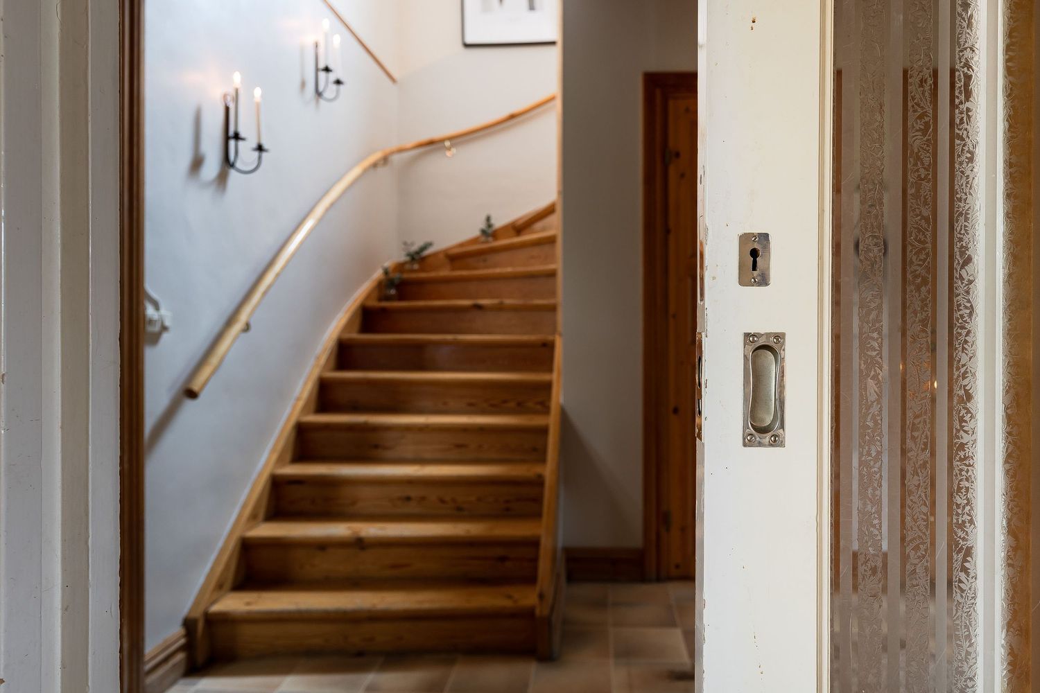 Wooden staircase with white walls and vintage wall sconce lighting in an elegant hallway interior.