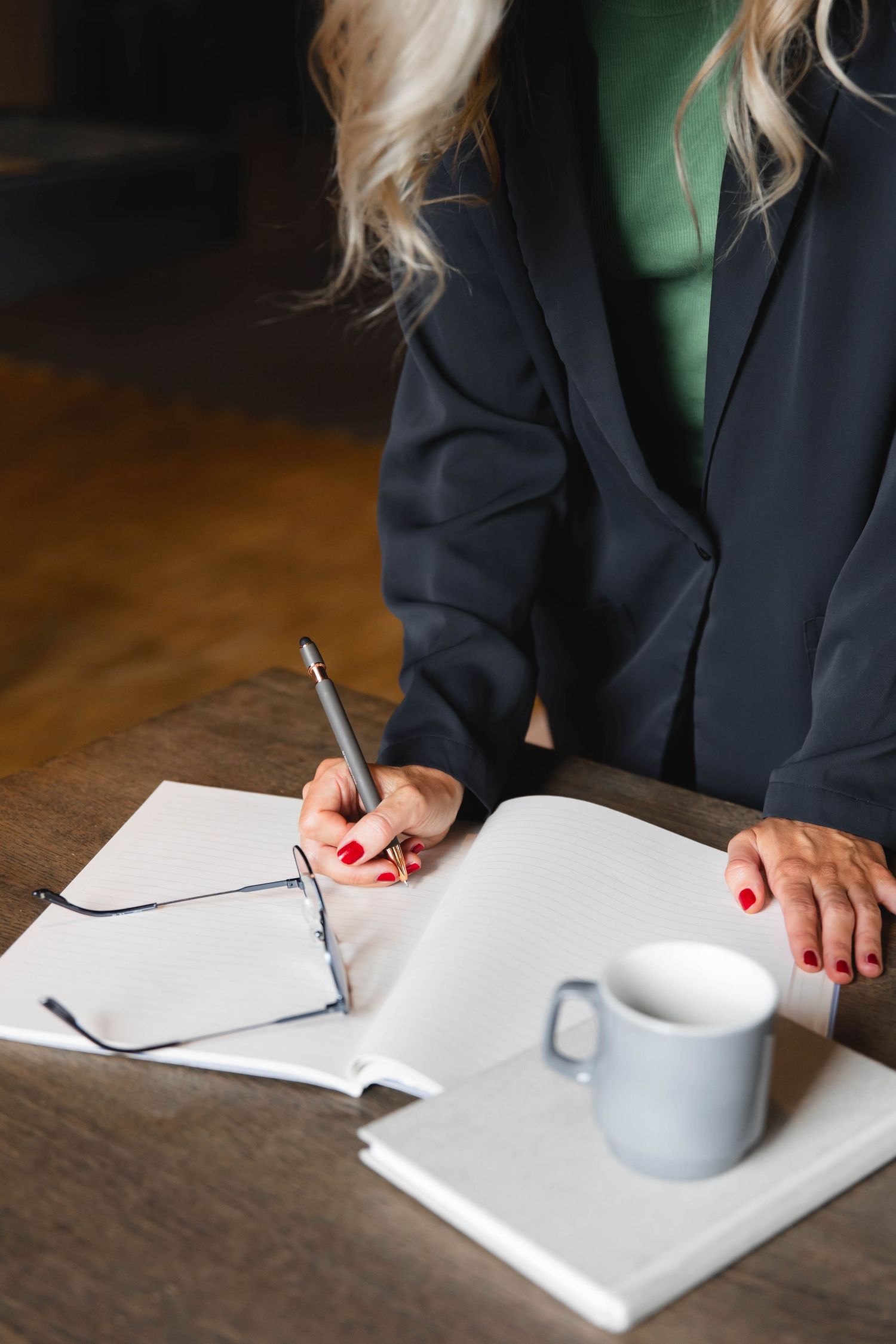 Person in navy blazer writing on white paper with a coffee cup on wooden table in sequence of shots.