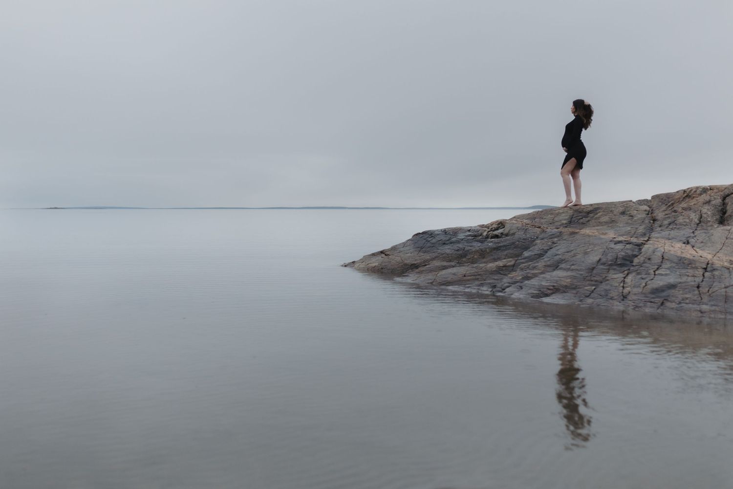 Person and dog walking along rocky coastal shoreline with dramatic cliffs and ocean views in background.