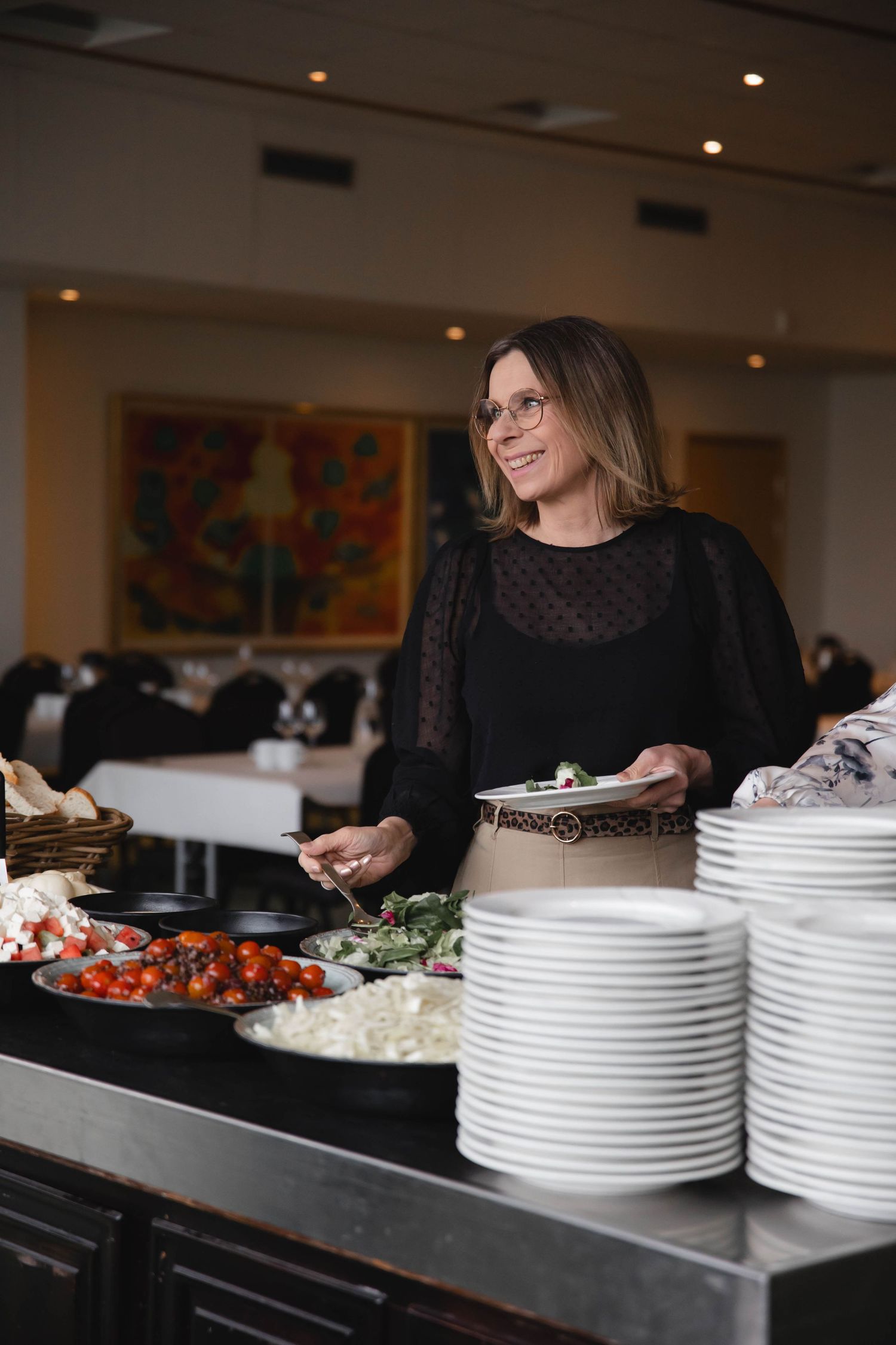 A person in black serving food at a buffet line with white plates stacked neatly on the counter.