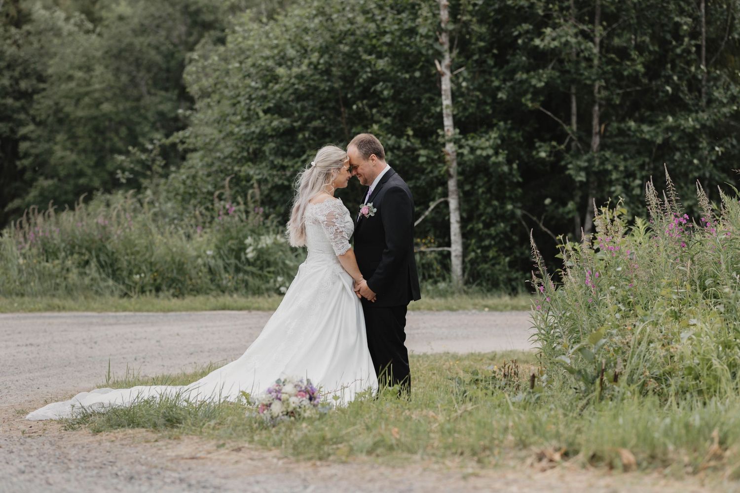 Romantic wedding couple embraces in a lush garden setting with wildflowers and trees creating a natural backdrop.