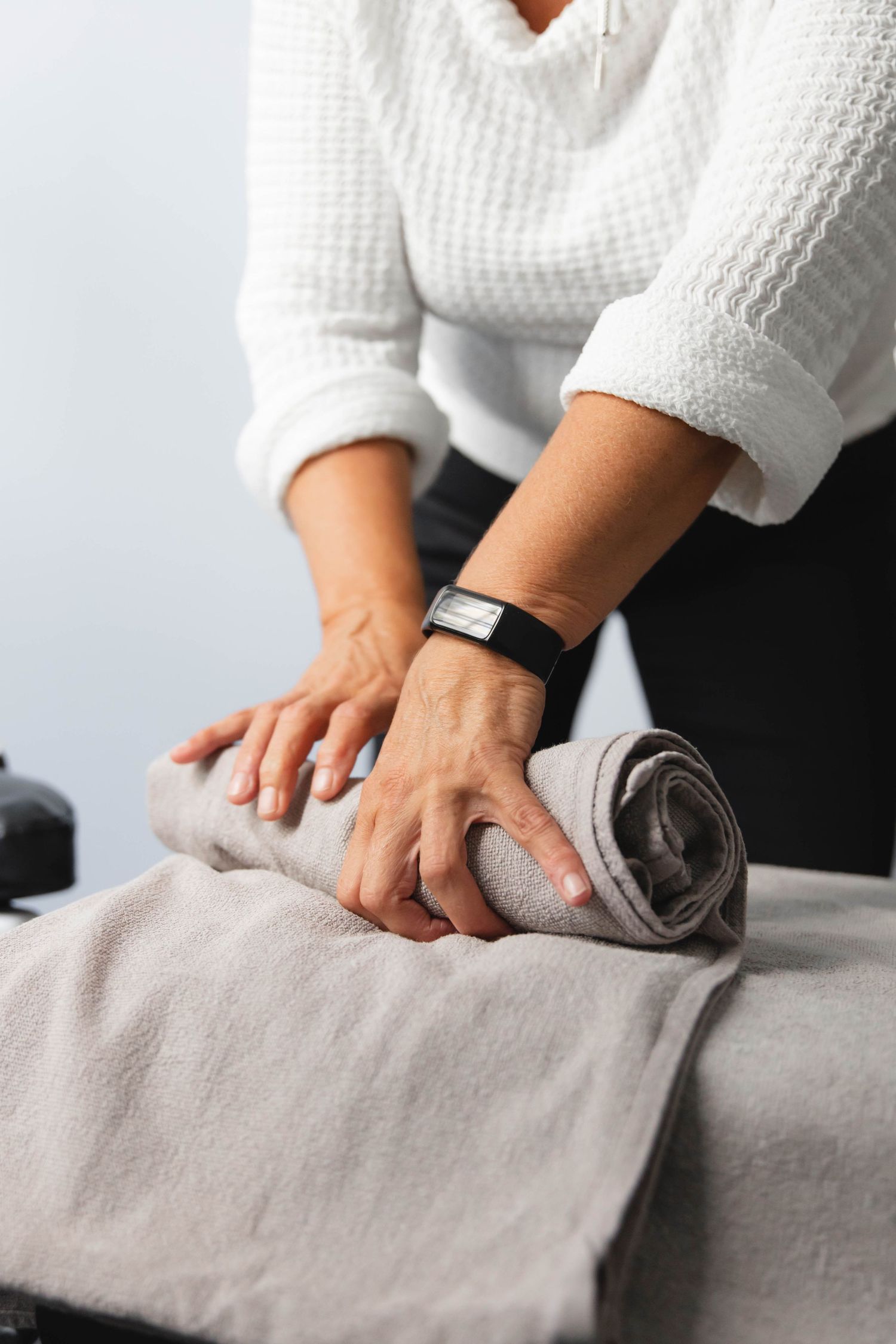 Hands in white sleeves pressing and smoothing out wrinkles on a gray fabric surface.