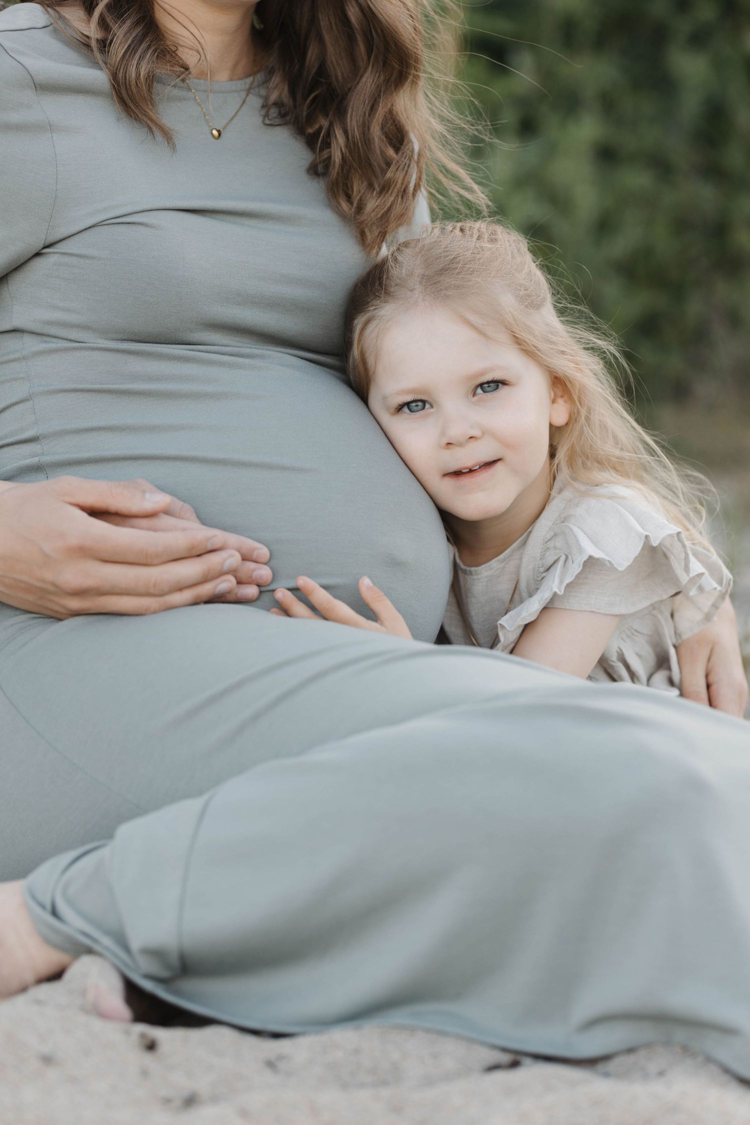 A tender maternity photo series showing a young child embracing a pregnant belly in soft, muted tones.