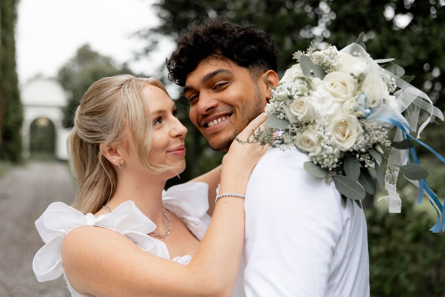 A romantic wedding couple shares intimate moments outdoors surrounded by white floral arrangements.