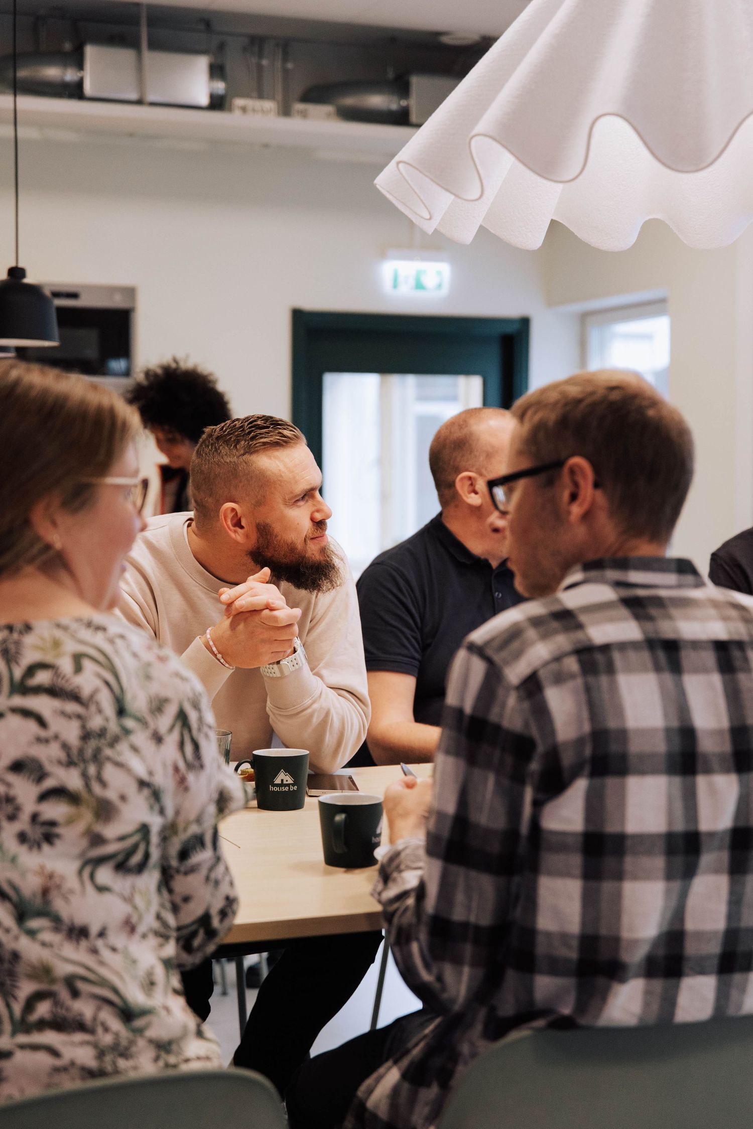 A group of people having a casual meeting around a table in a modern office space with pendant lighting.