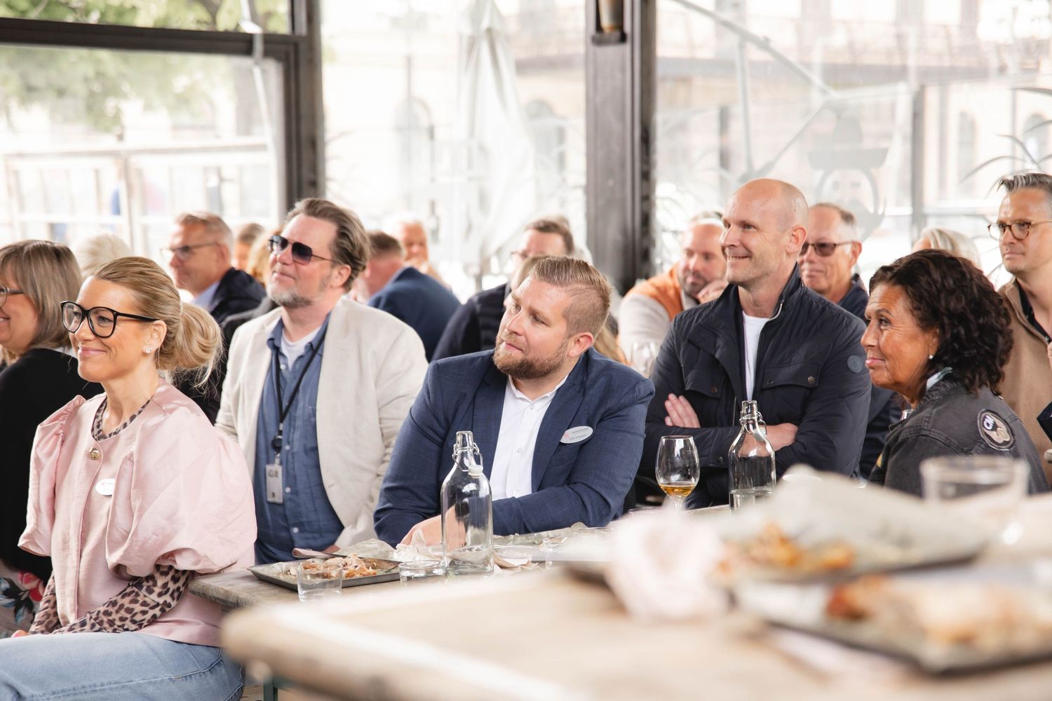Attentive audience members watch intently during a professional event while seated at tables with wine glasses.