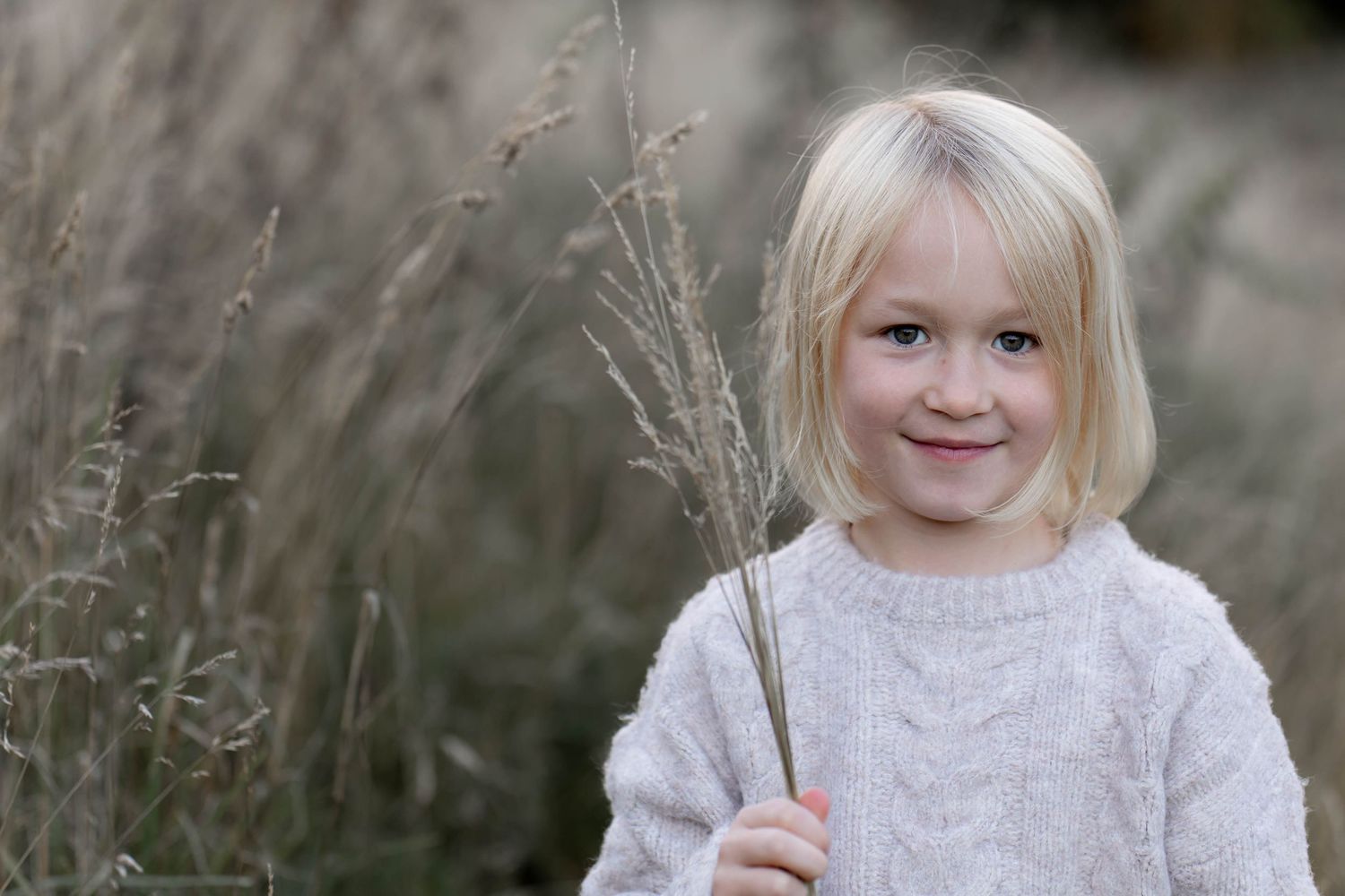 A child wearing a cozy white knit sweater plays outdoors in a natural setting during autumn.
