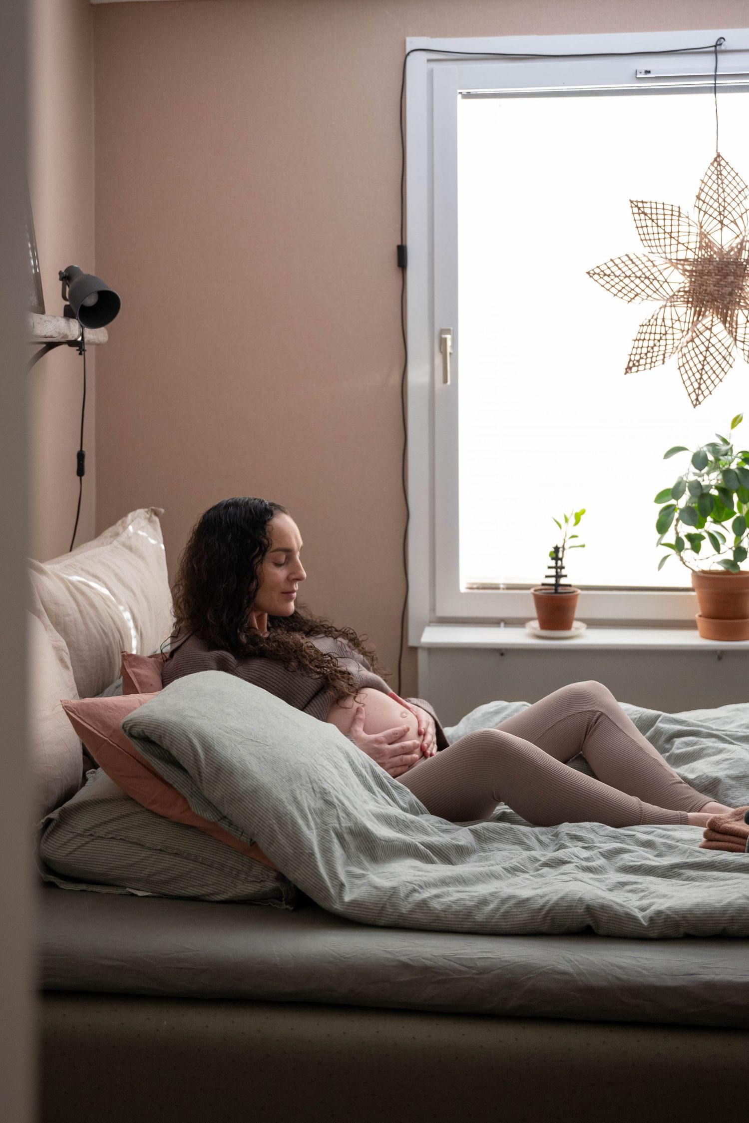 A series of four photos showing someone resting on a bed near a window with natural light and houseplants.