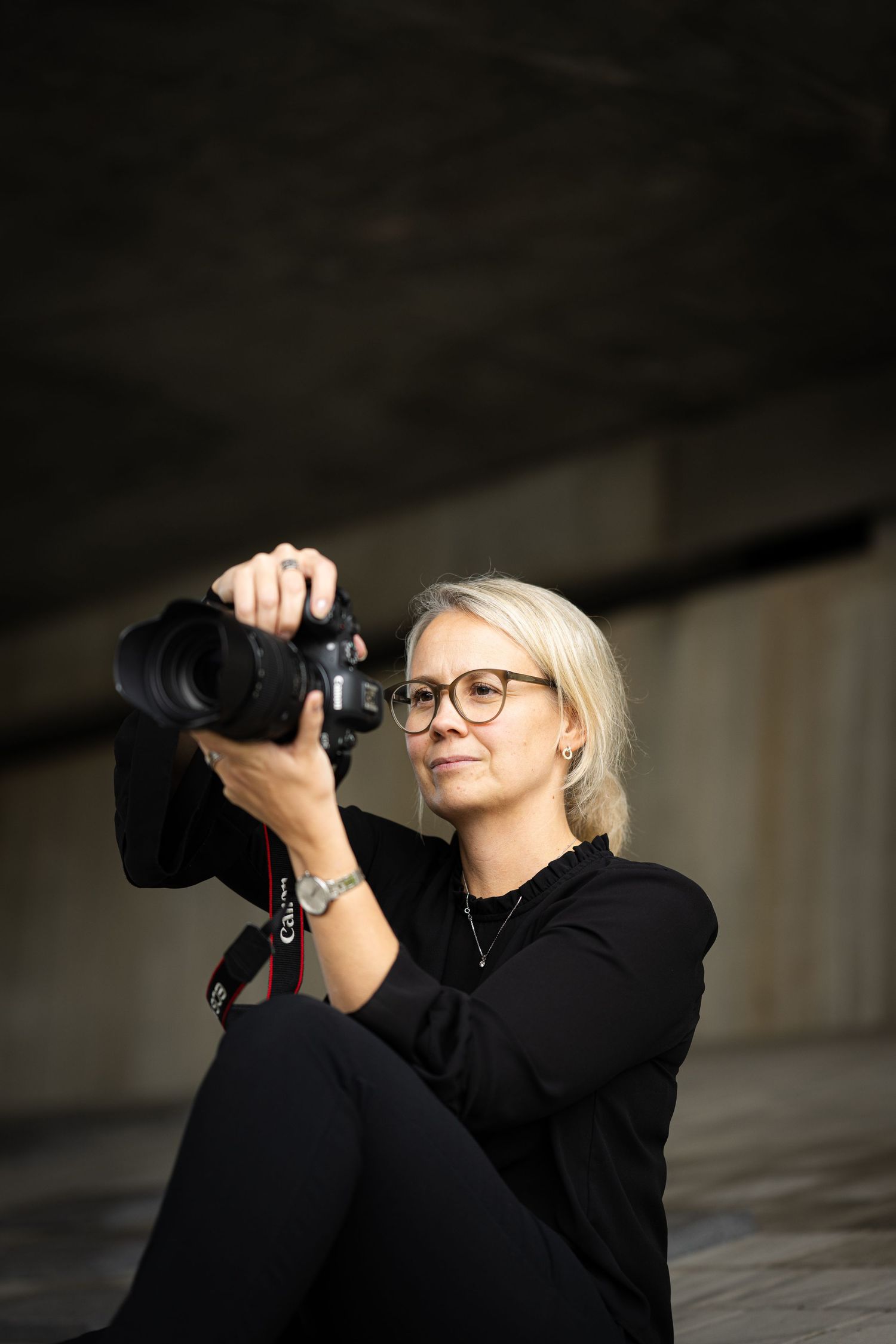 A photographer in black clothing and glasses aims a professional camera with telephoto lens upward while shooting.
