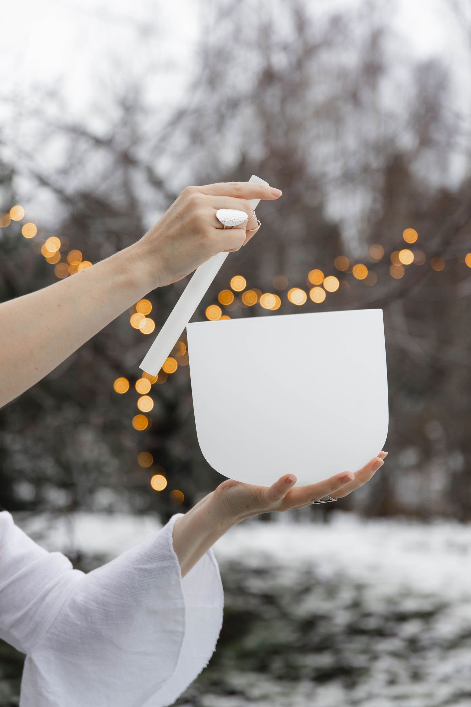 Hands holding white paper against snowy winter background with bokeh lights creating dreamy atmosphere.