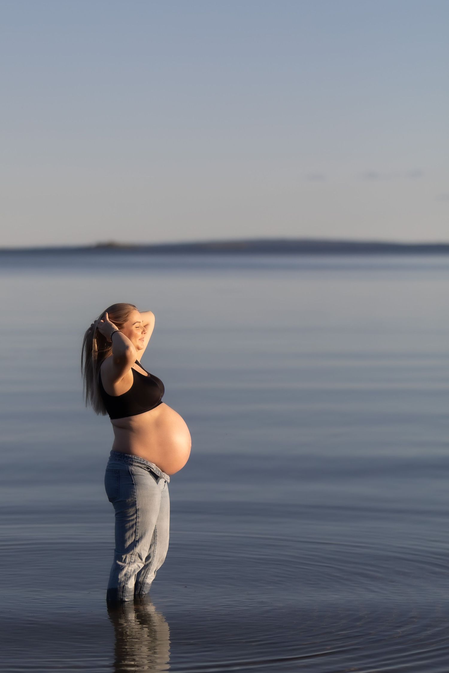 Person standing in calm water at sunset creates ripples while looking up at the serene sky in a contemplative pose.
