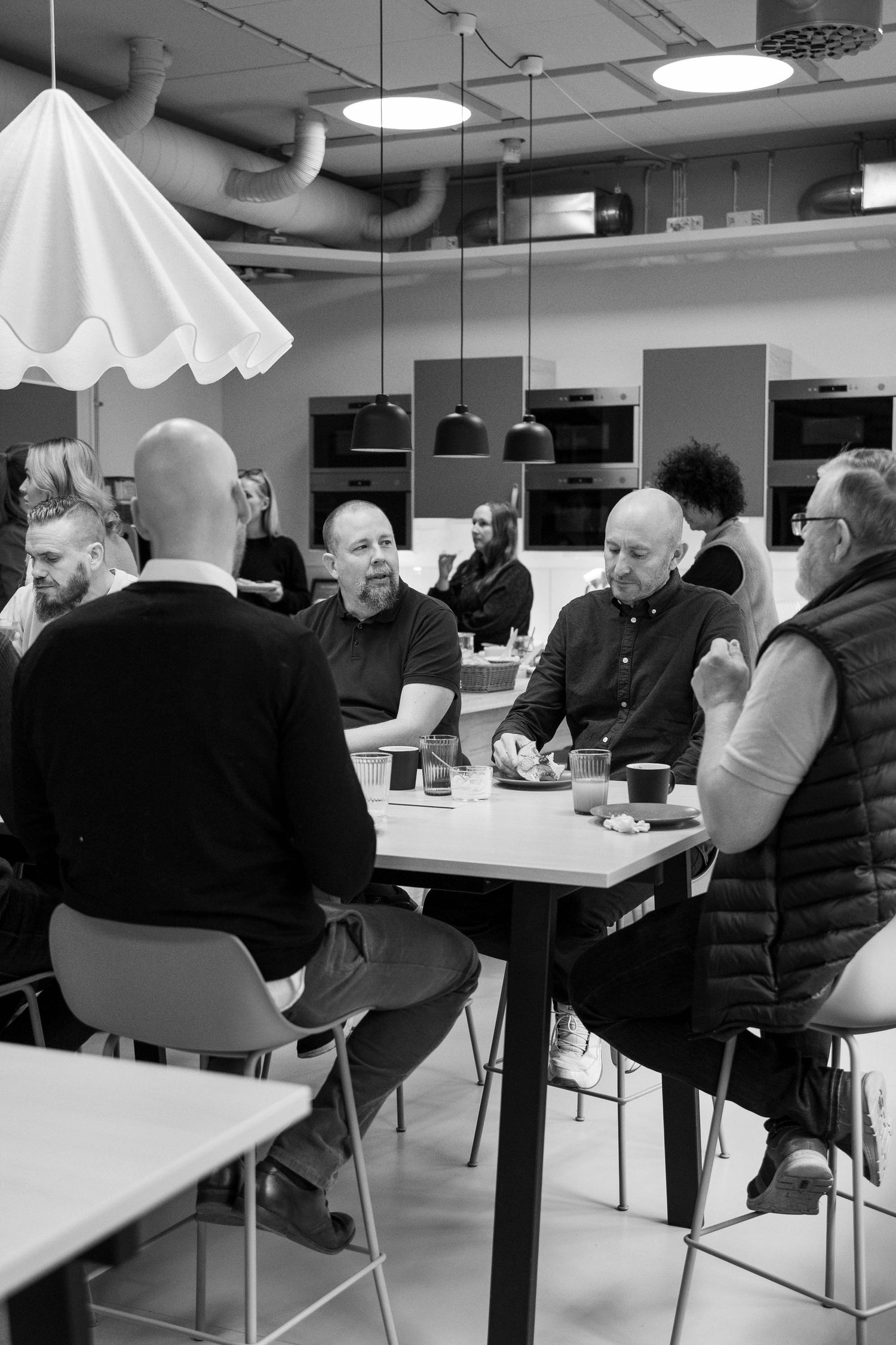 People seated at tables in a cafeteria or break room having conversations in black and white photography.