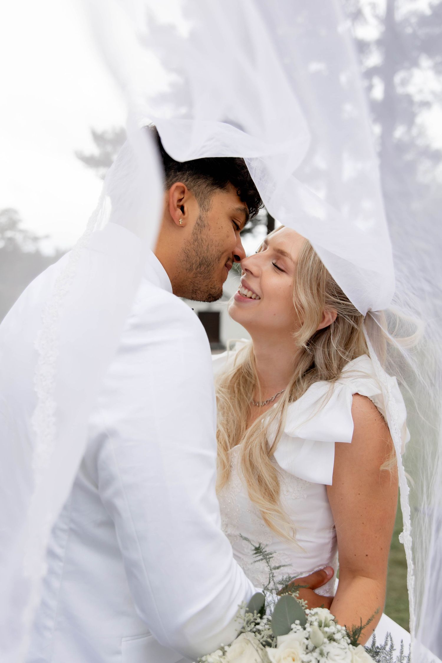 A bride and groom share a romantic moment under a flowing white veil on their wedding day.