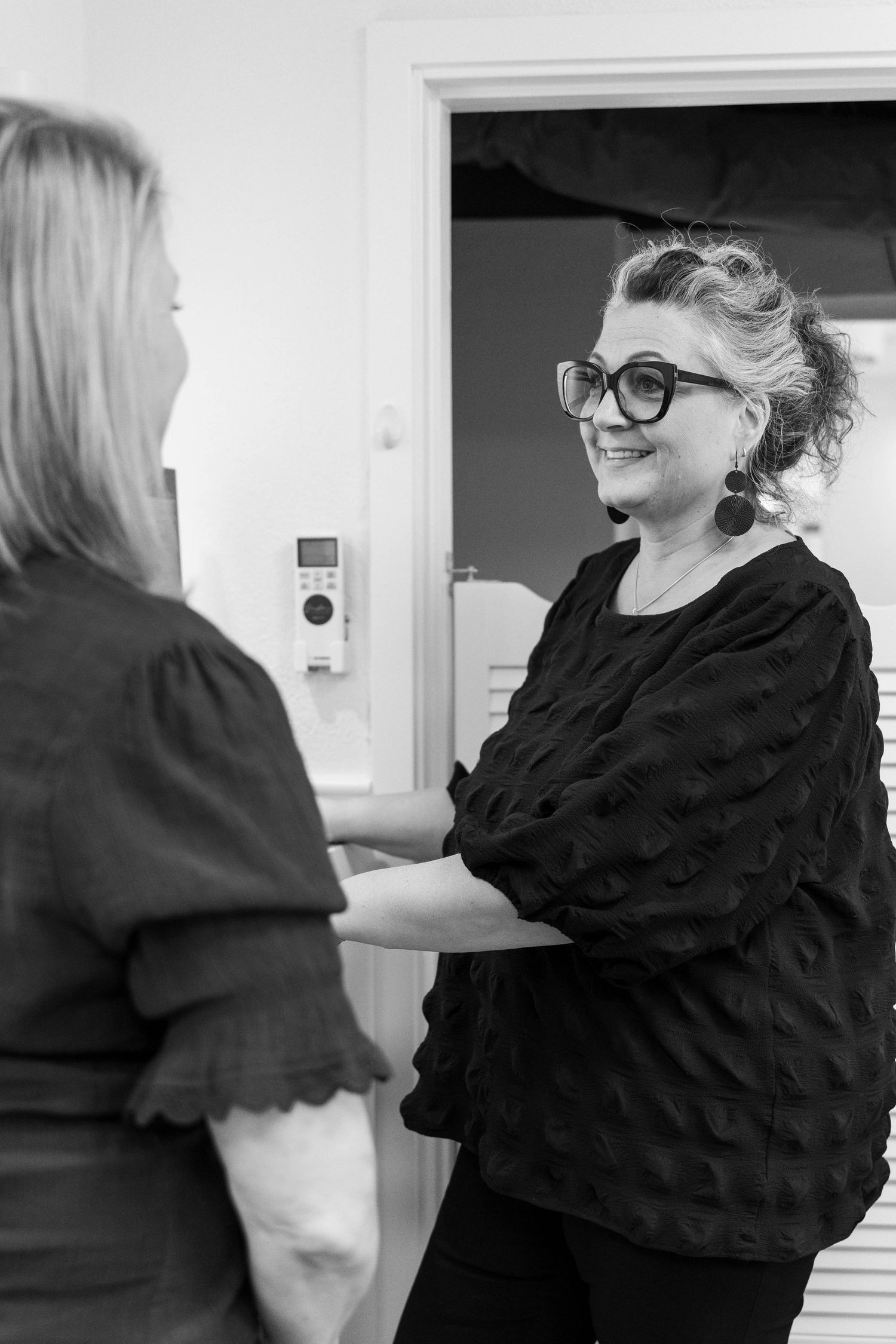 Two people in black clothing having an animated conversation in a bright indoor space.