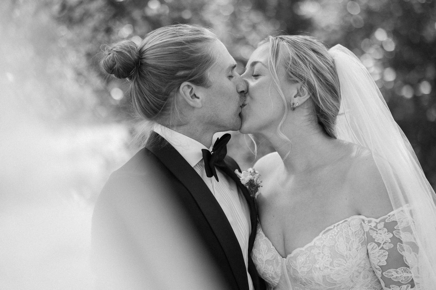 Black and white photo of a bride and groom sharing a kiss on their wedding day, bride wearing a veil.