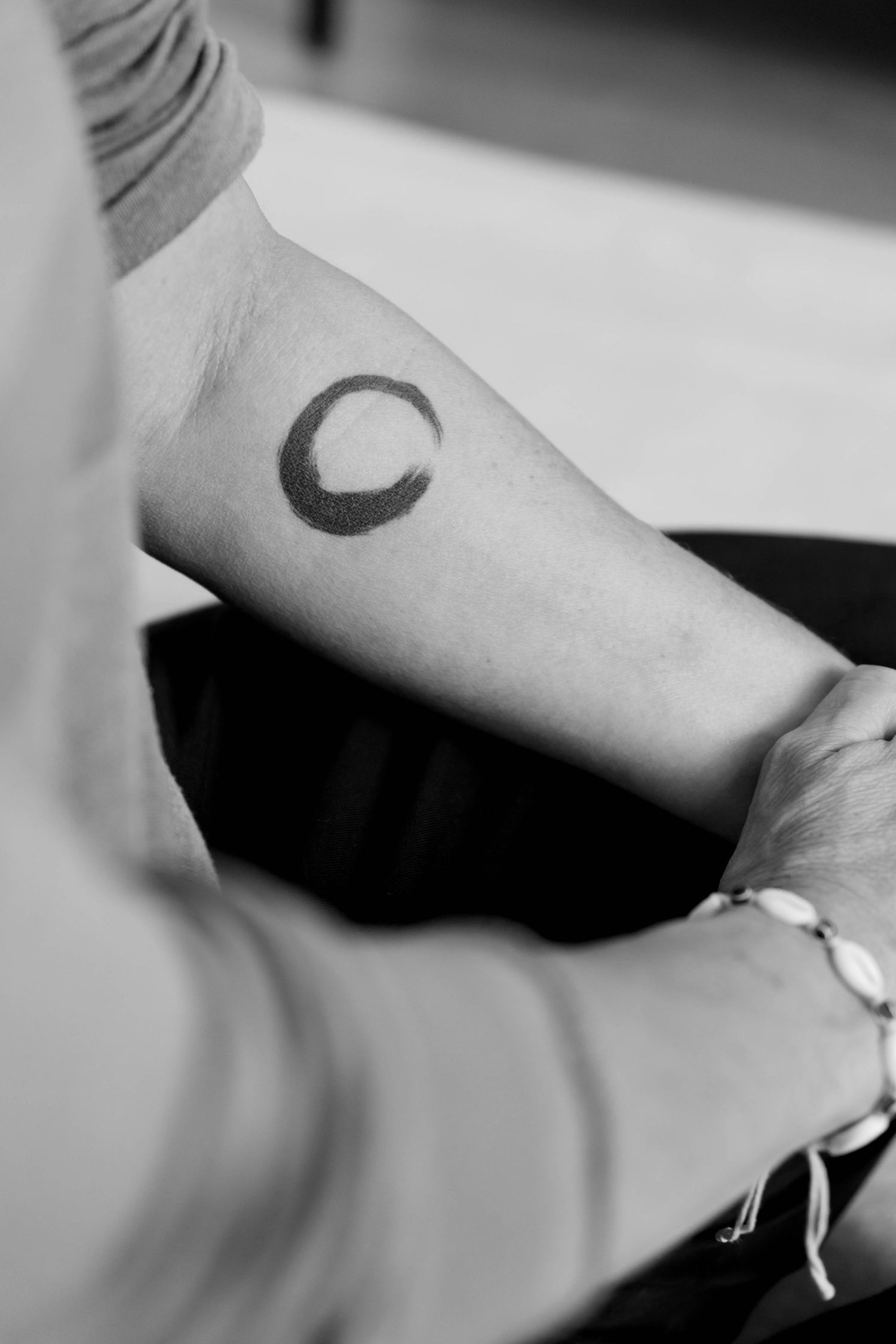 A small crescent moon tattoo design shown in black ink on a person's arm in a minimalist style.