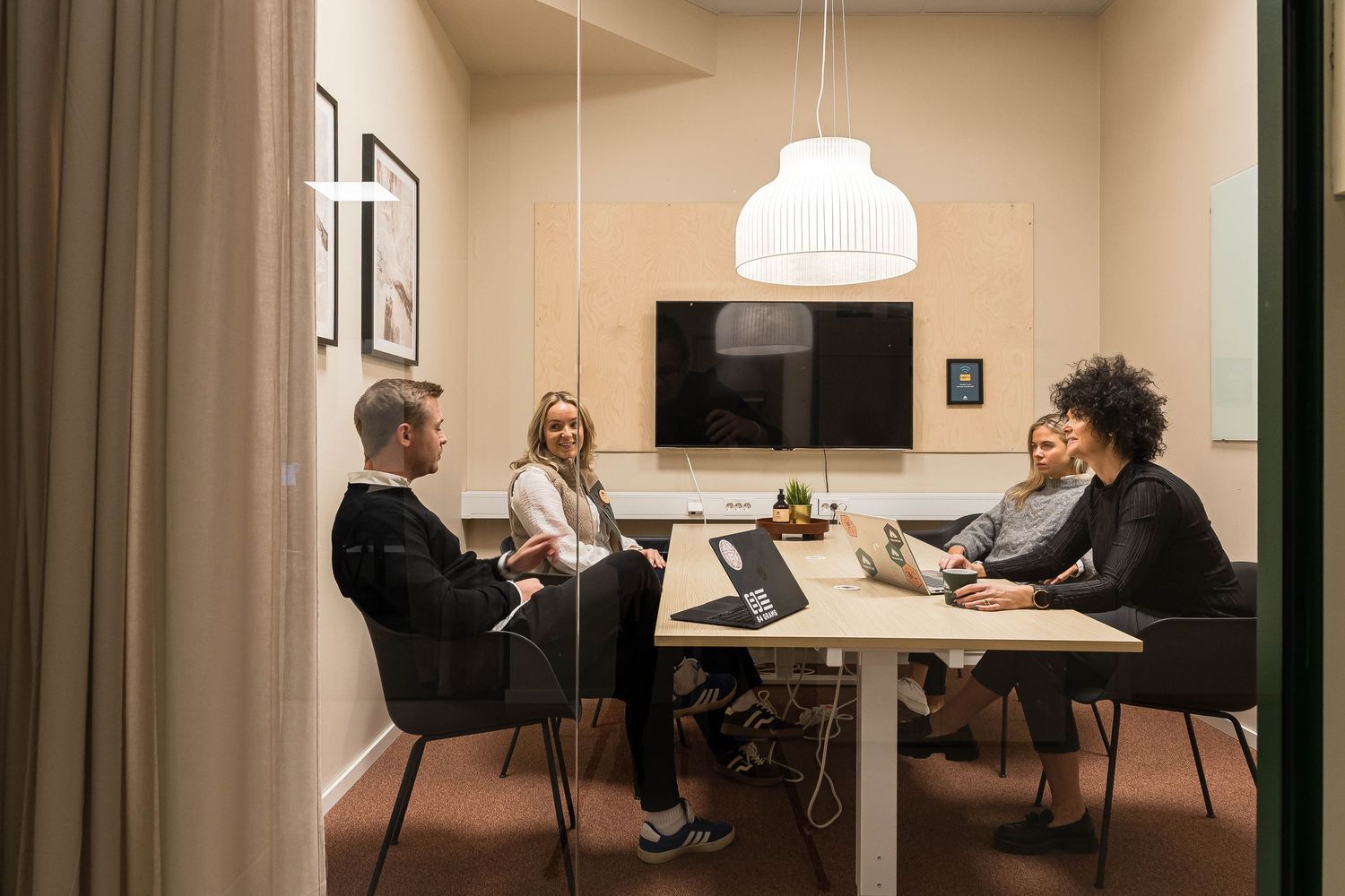 People working and meeting in a modern office space with white tables and chairs under pendant lighting.