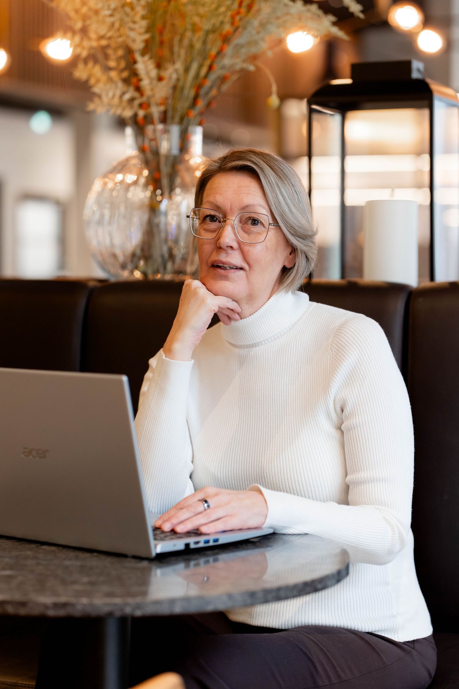 A person in a white sweater sits at a desk with a laptop in a modern office space with warm lighting.