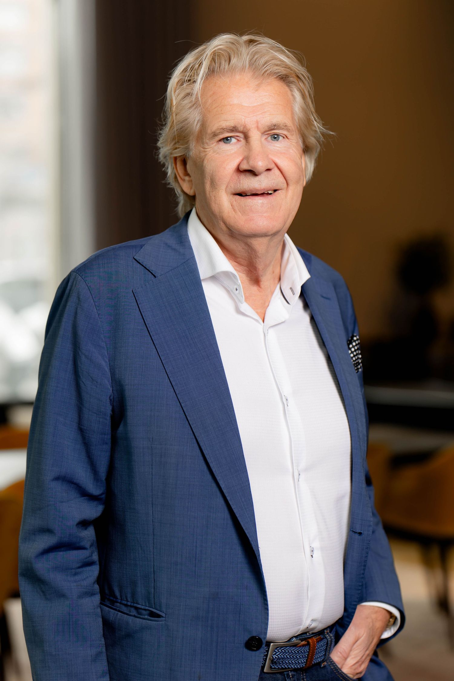 Person in a navy blue suit and white shirt smiling while looking to the side in an office setting.