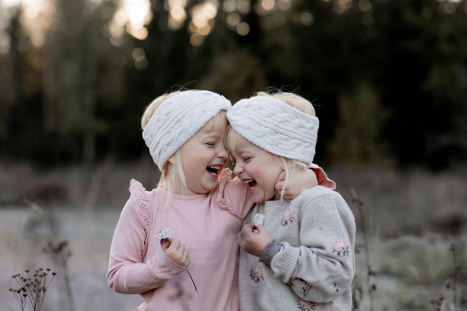 Two children in matching pink and white outfits sitting together outdoors in a natural setting.