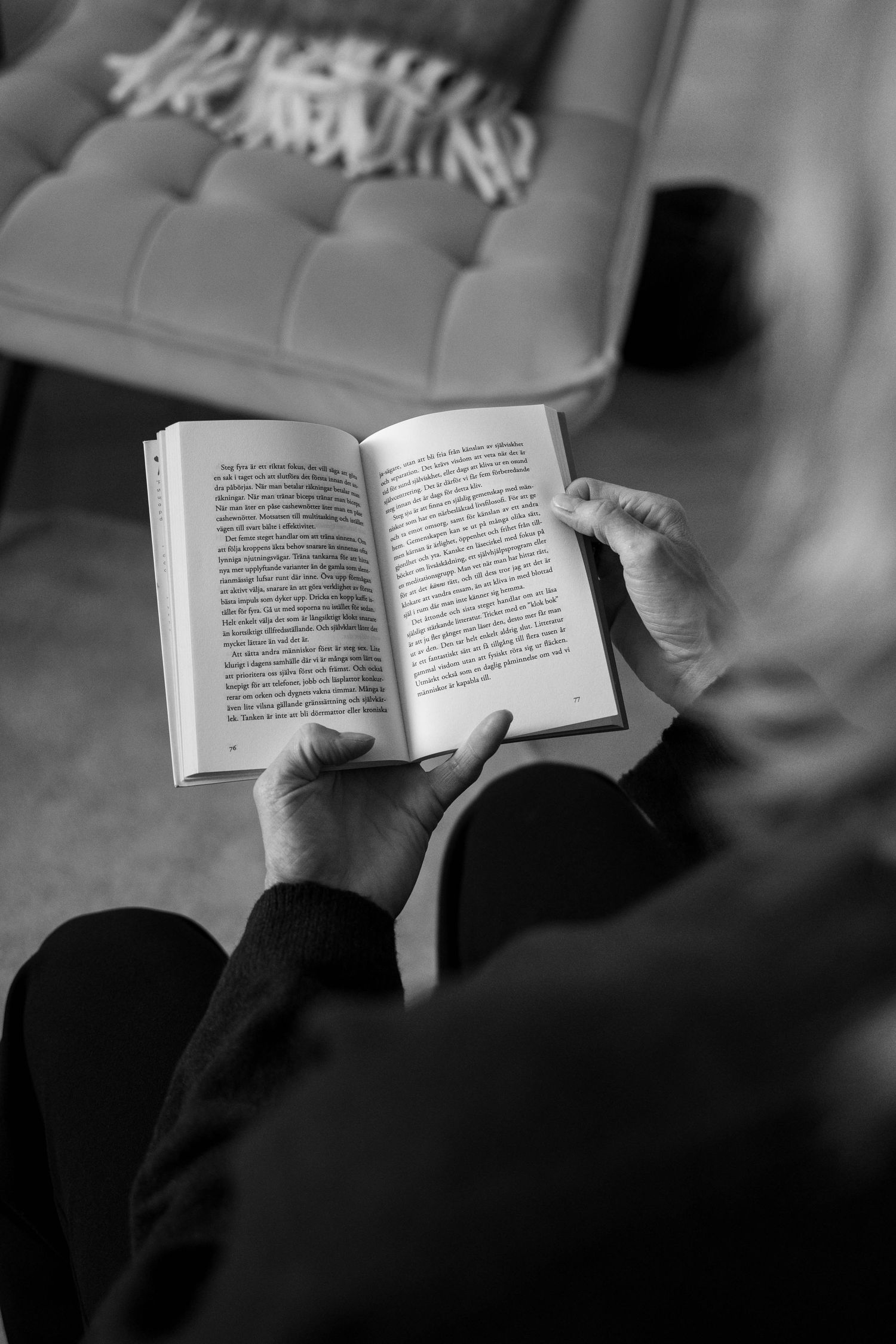 A person reading a paperback book while relaxing on a couch, captured in black and white photography.