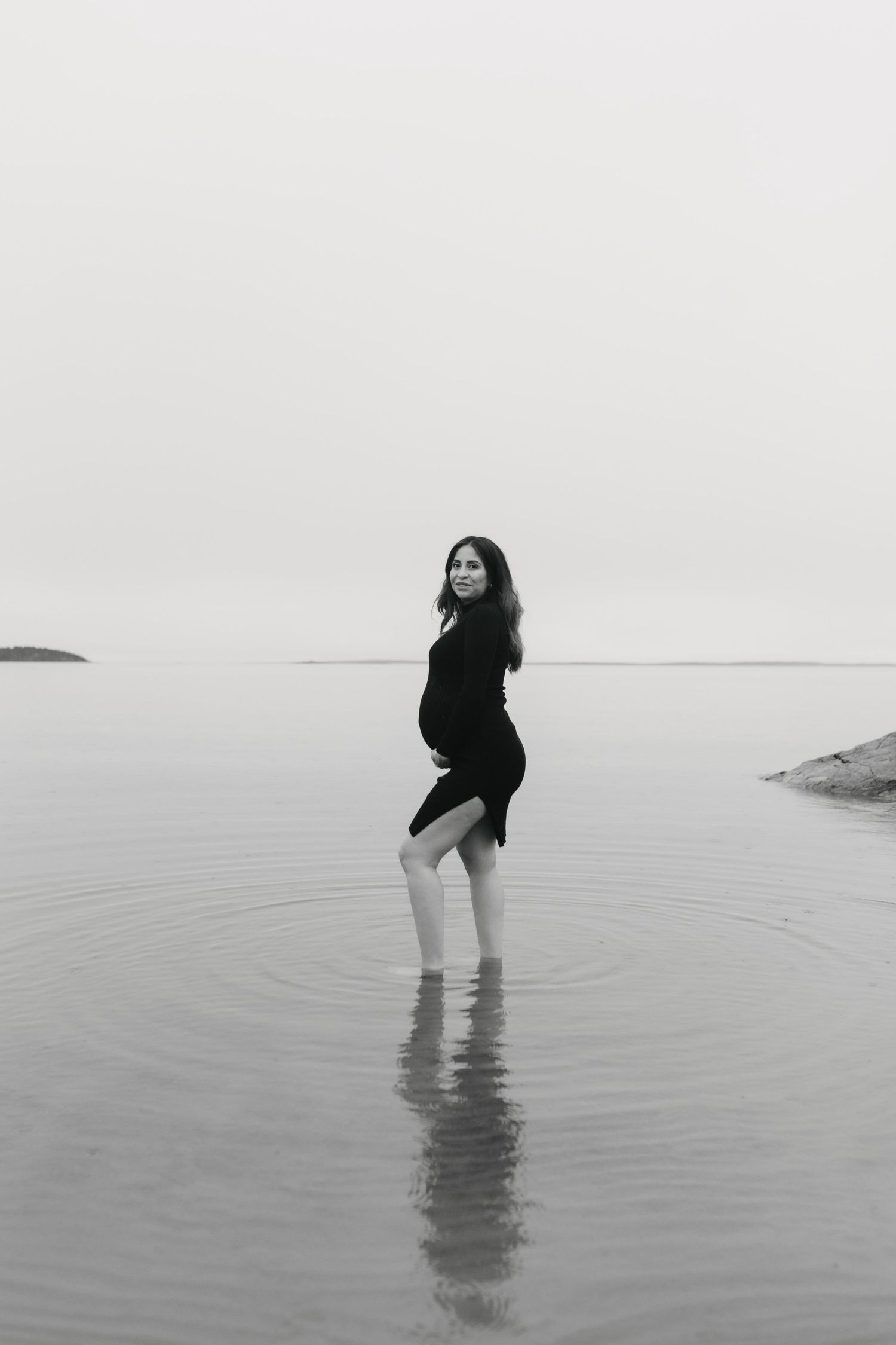 A person in black clothing wades through shallow water in a minimalist black and white seascape series.