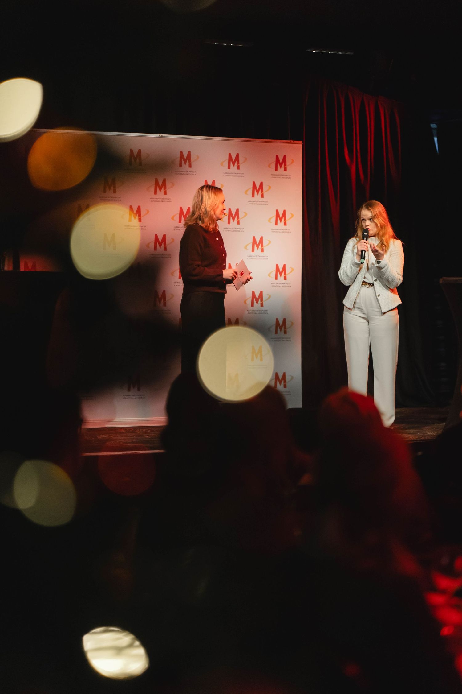 A dark stage performance with dramatic red lighting and white spotlights creating an atmospheric ambiance.