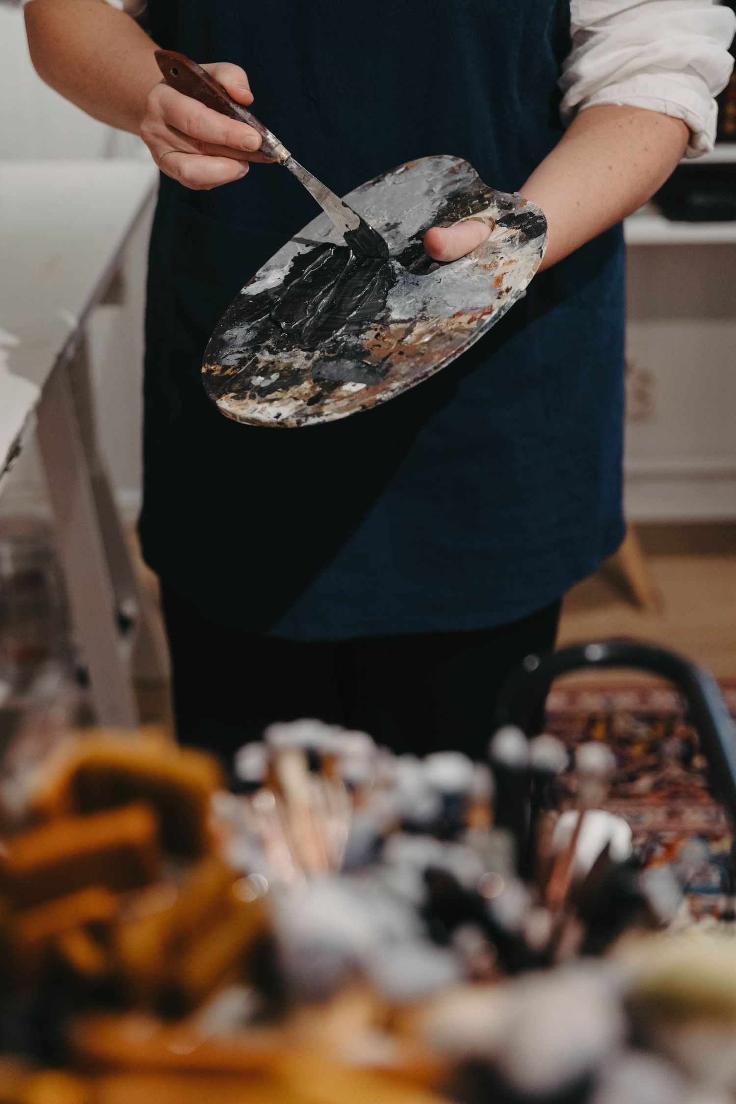 Close-up of hands mixing paint colors on a palette with palette knife against dark background.