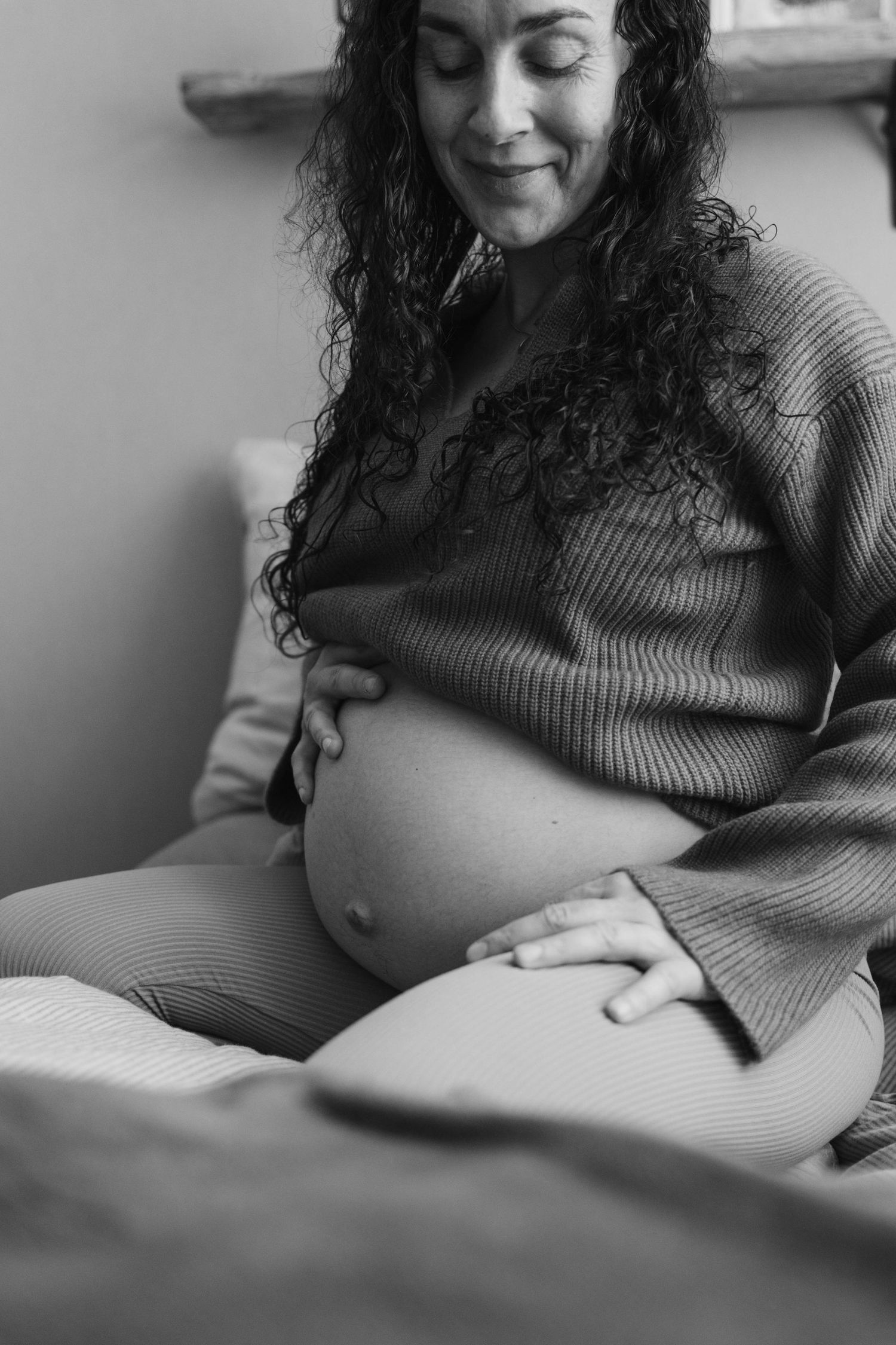 Black and white maternity photo series showing a pregnant woman in a ribbed sweater cradling her baby bump.