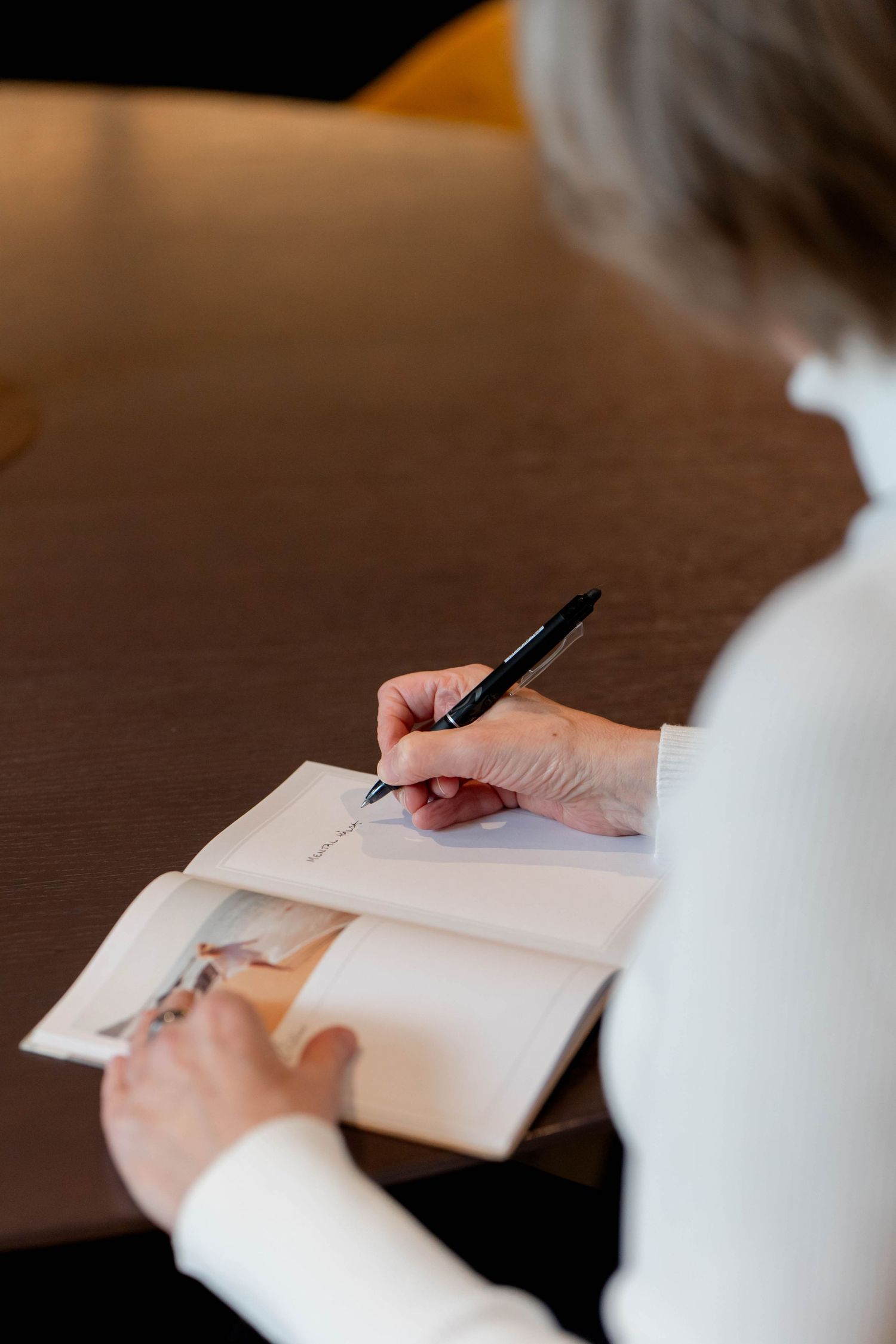 Close-up of hands signing a document with a black pen on a wooden surface.