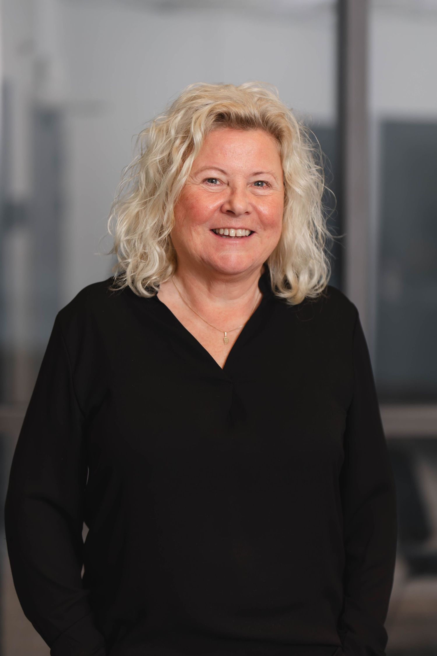 Professional headshot series showing different expressions while wearing a black top against a blurred background.
