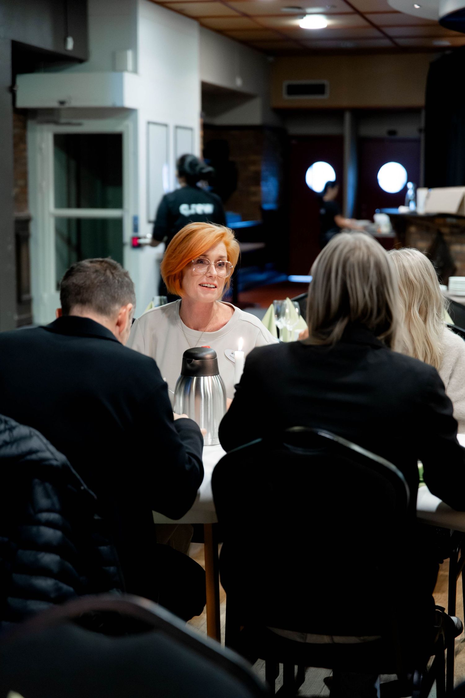 People sit at tables in a dimly lit restaurant interior with overhead lighting creating a cozy ambiance.