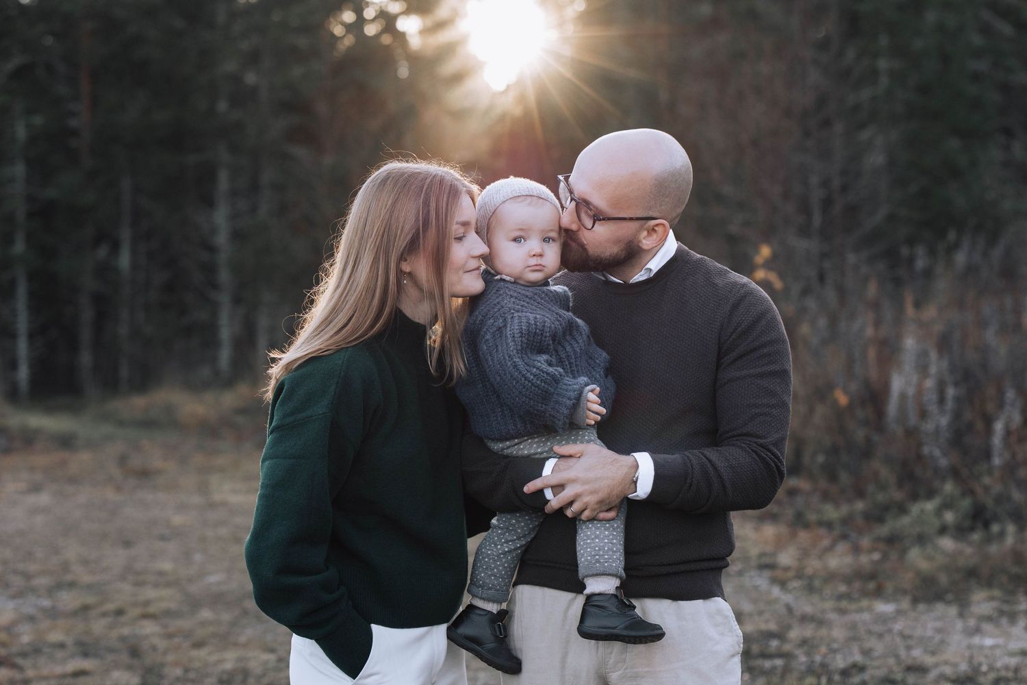 A family embraces in a sunlit forest setting during an outdoor photo session at golden hour.