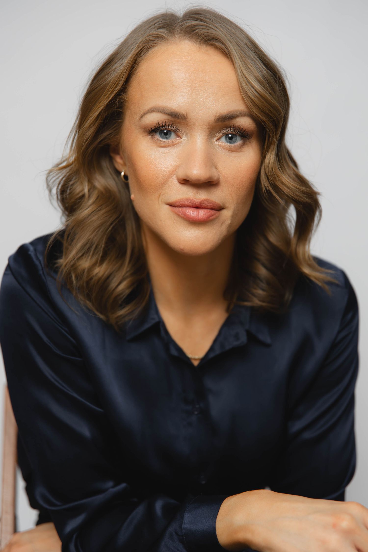 A series of five headshots showing someone in a navy blue top with wavy brown hair against a light background.