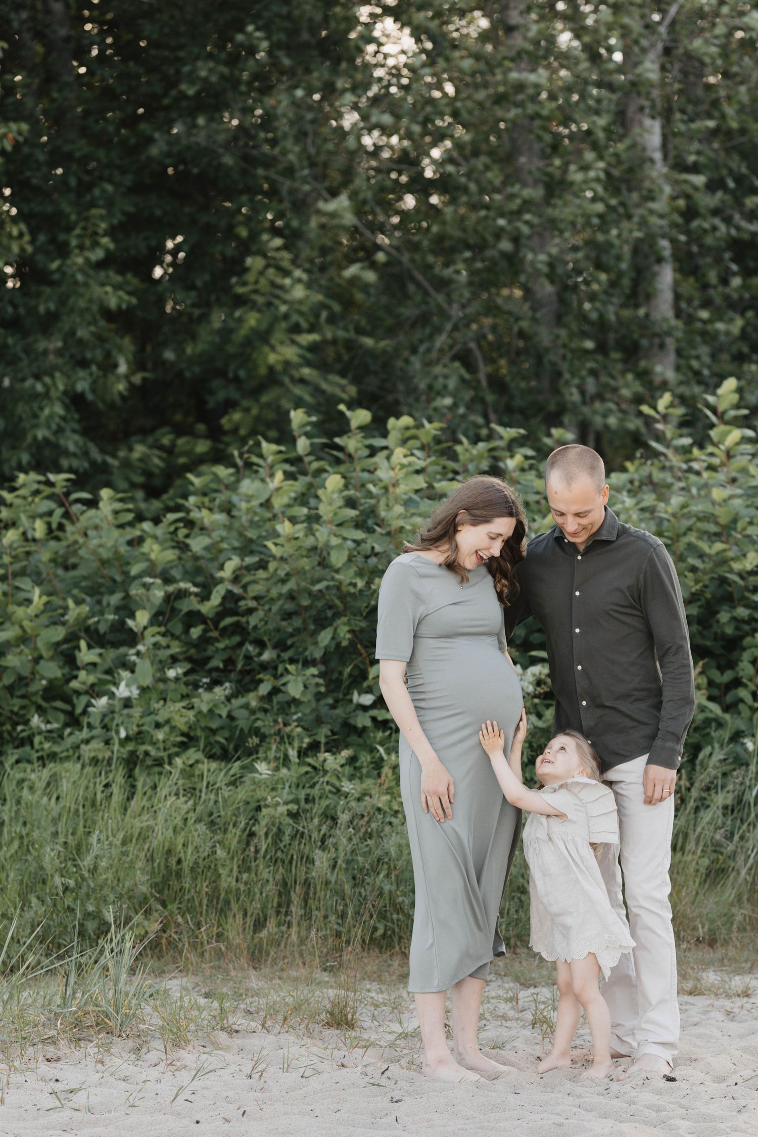 Family of three walking together on sandy beach path surrounded by lush green foliage and trees.